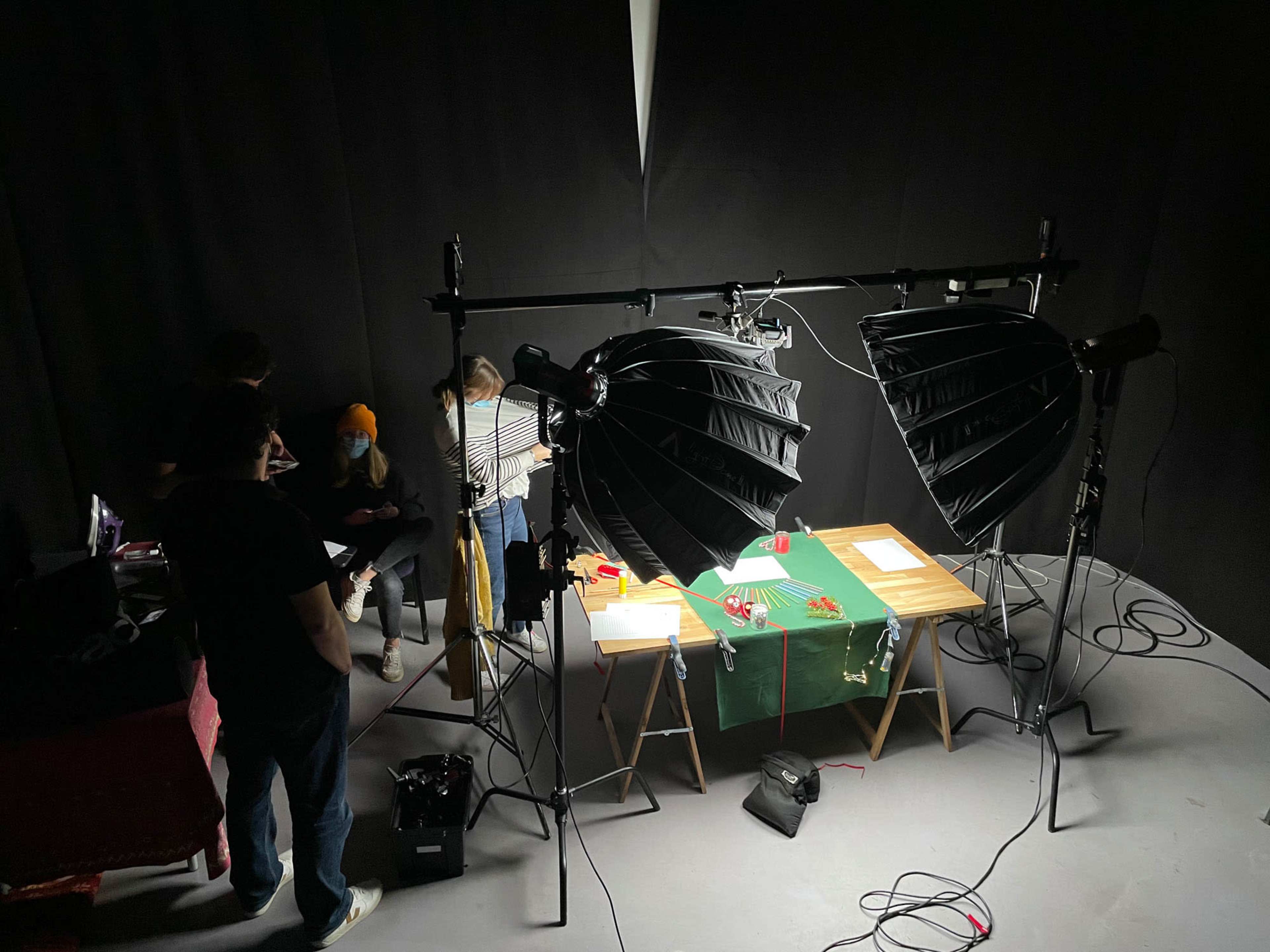 A group of people is setting up a photography scene with large softbox lights and a table covered in a green cloth.