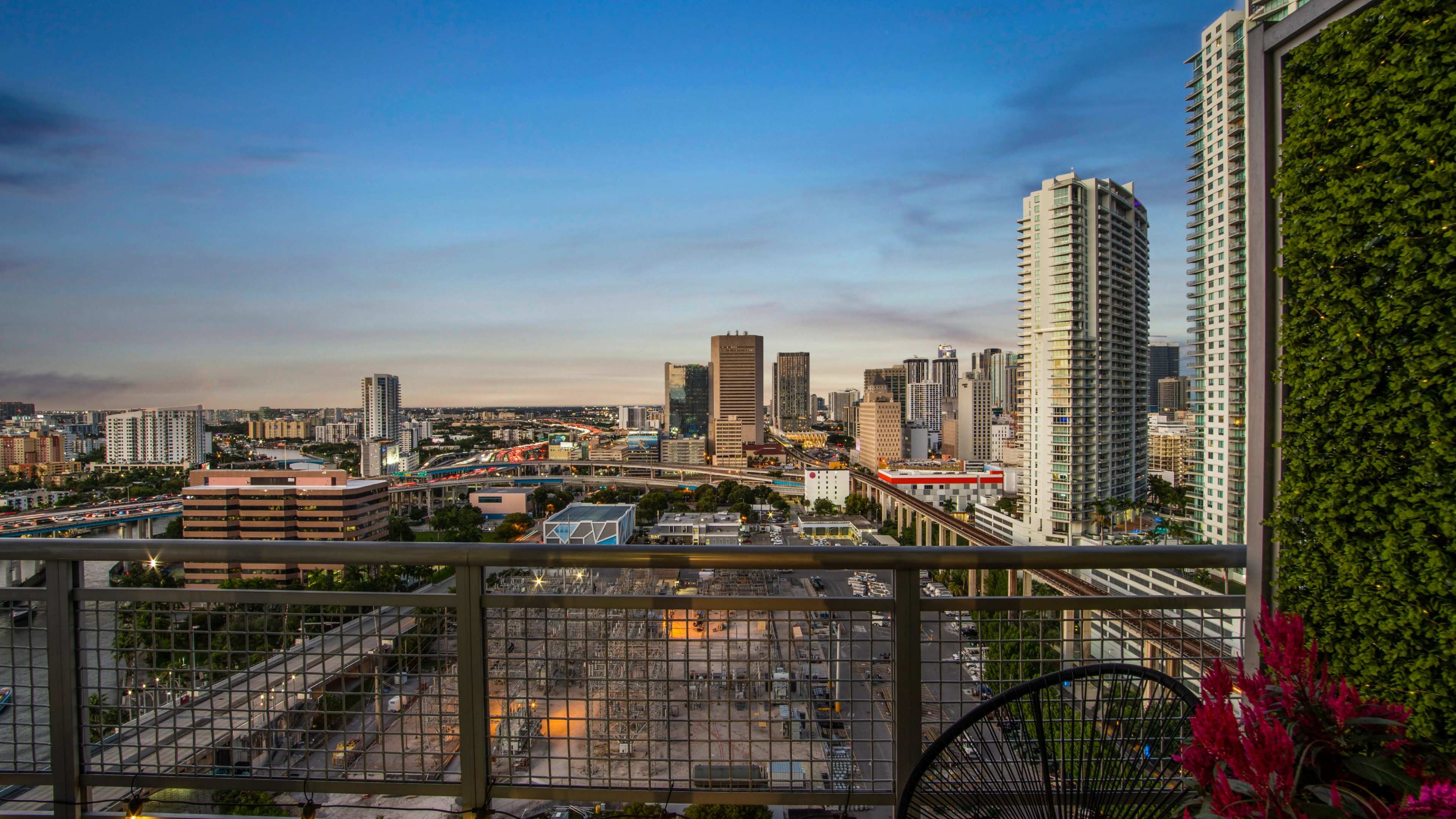 A city skyline view from a high-rise balcony, highlighting modern buildings and urban infrastructure under a clear blue sky.