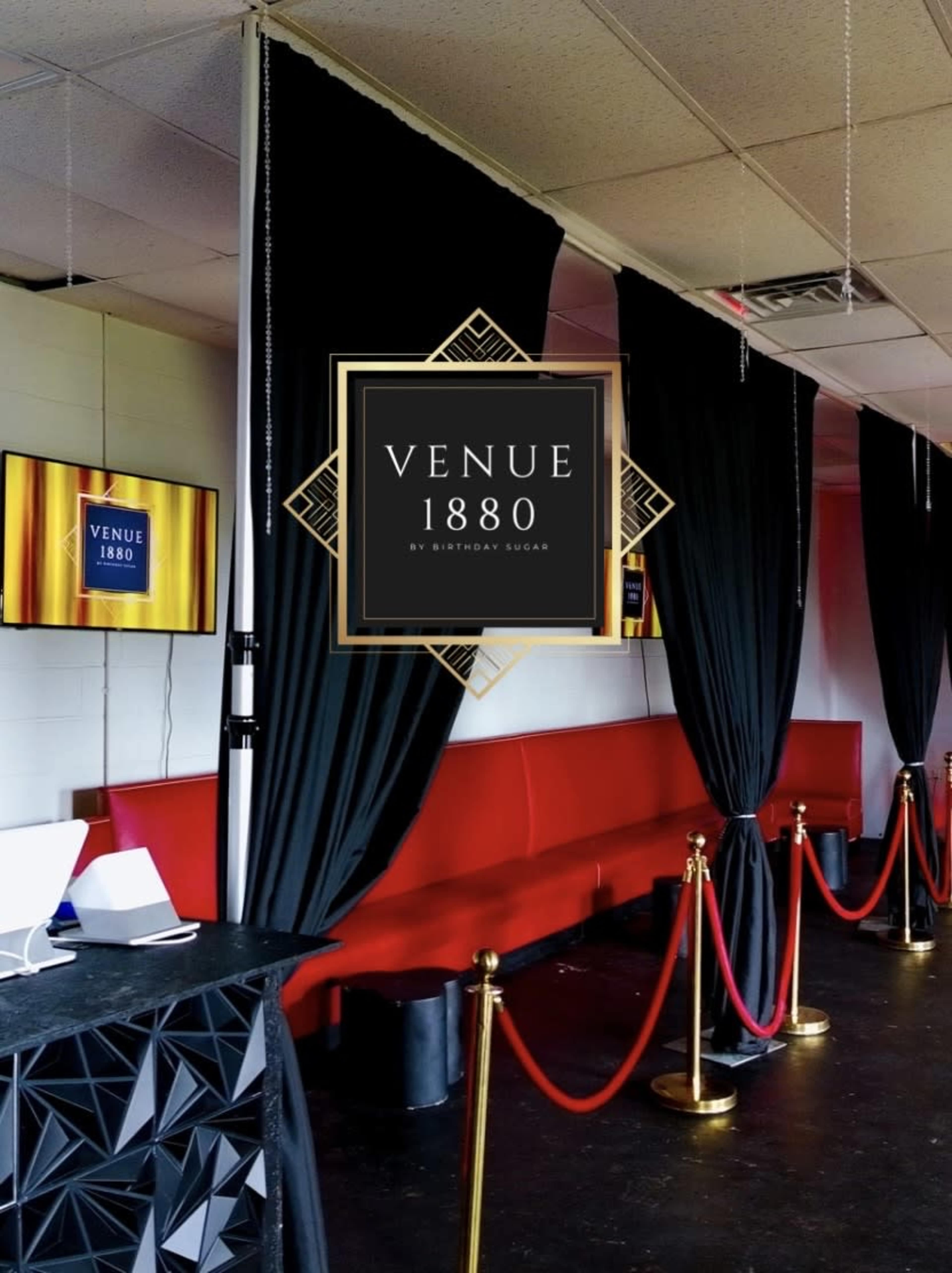 The image shows the interior of a venue with red seating, black curtains, and a sign displaying "Venue 1880" against a modern decor backdrop.
