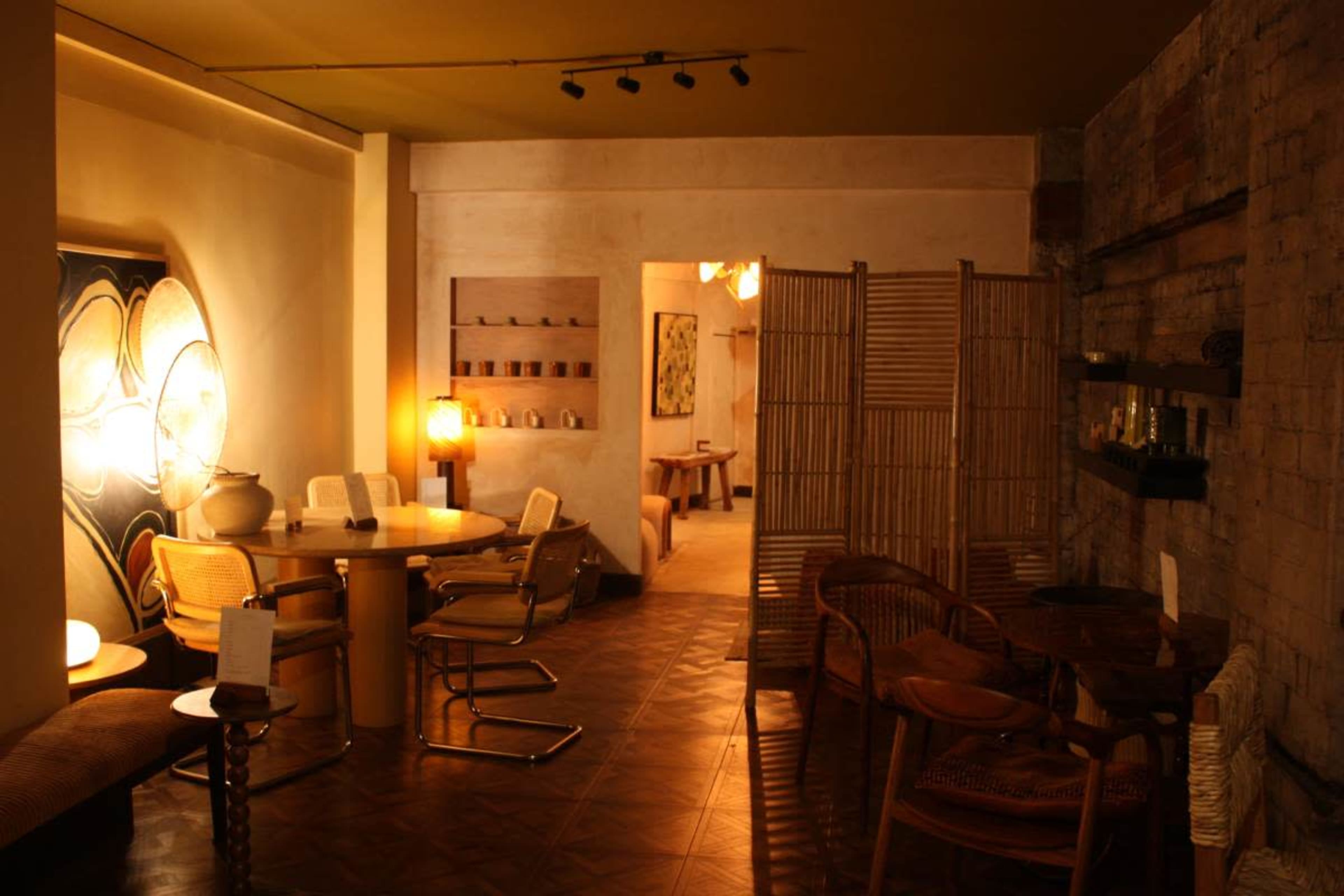 A cozy, minimalist interior space featuring a dining area with a round table and chairs, wooden partitions, and various decorative elements on the walls.