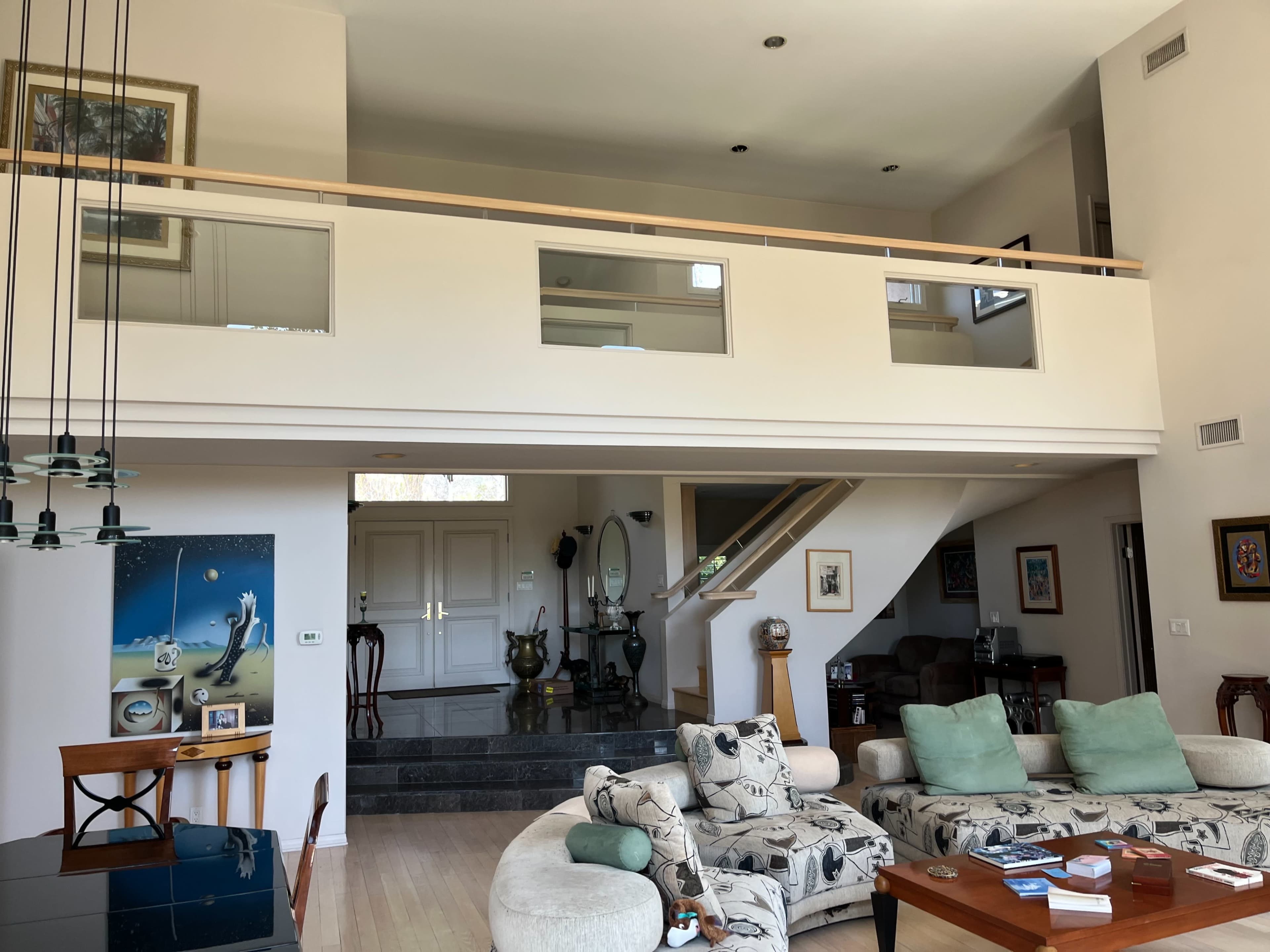 The image shows a spacious, modern living area with a staircase leading to an upper level and large windows allowing natural light to enter.