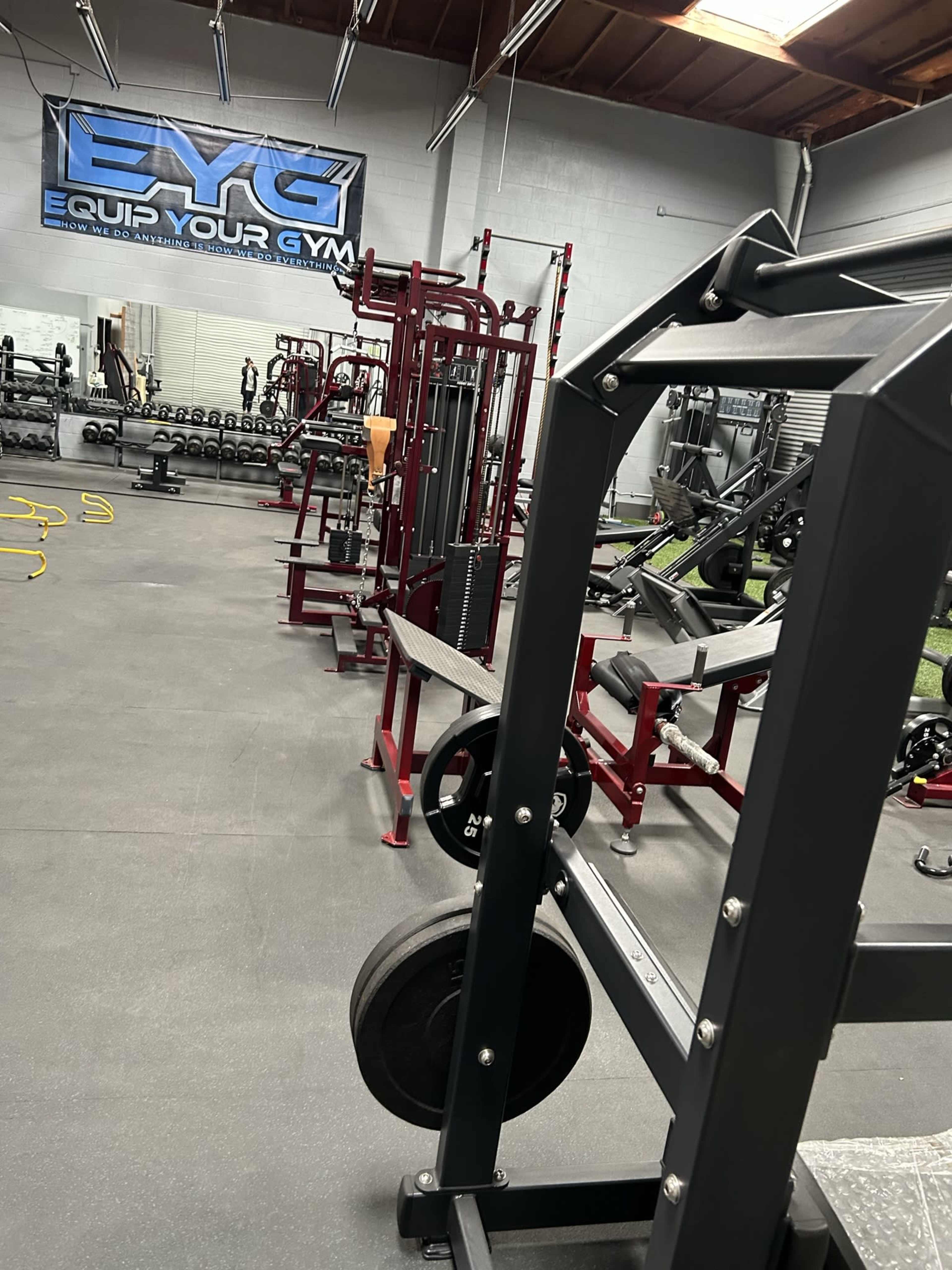 A fitness gym interior with various weightlifting machines and equipment aligned in rows.