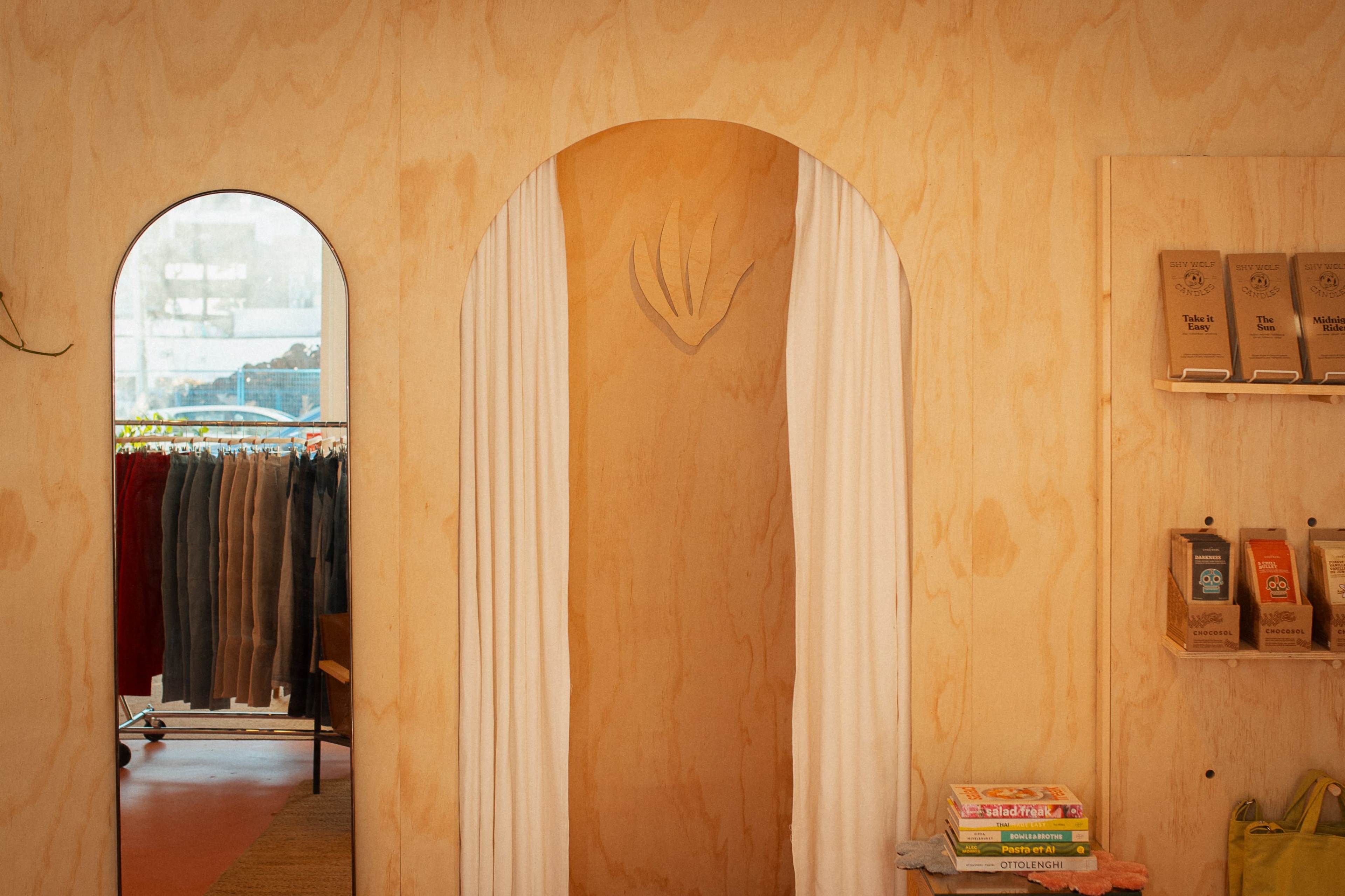 An interior of a retail space with a wooden archway, a mirror, and clothing racks in the background.