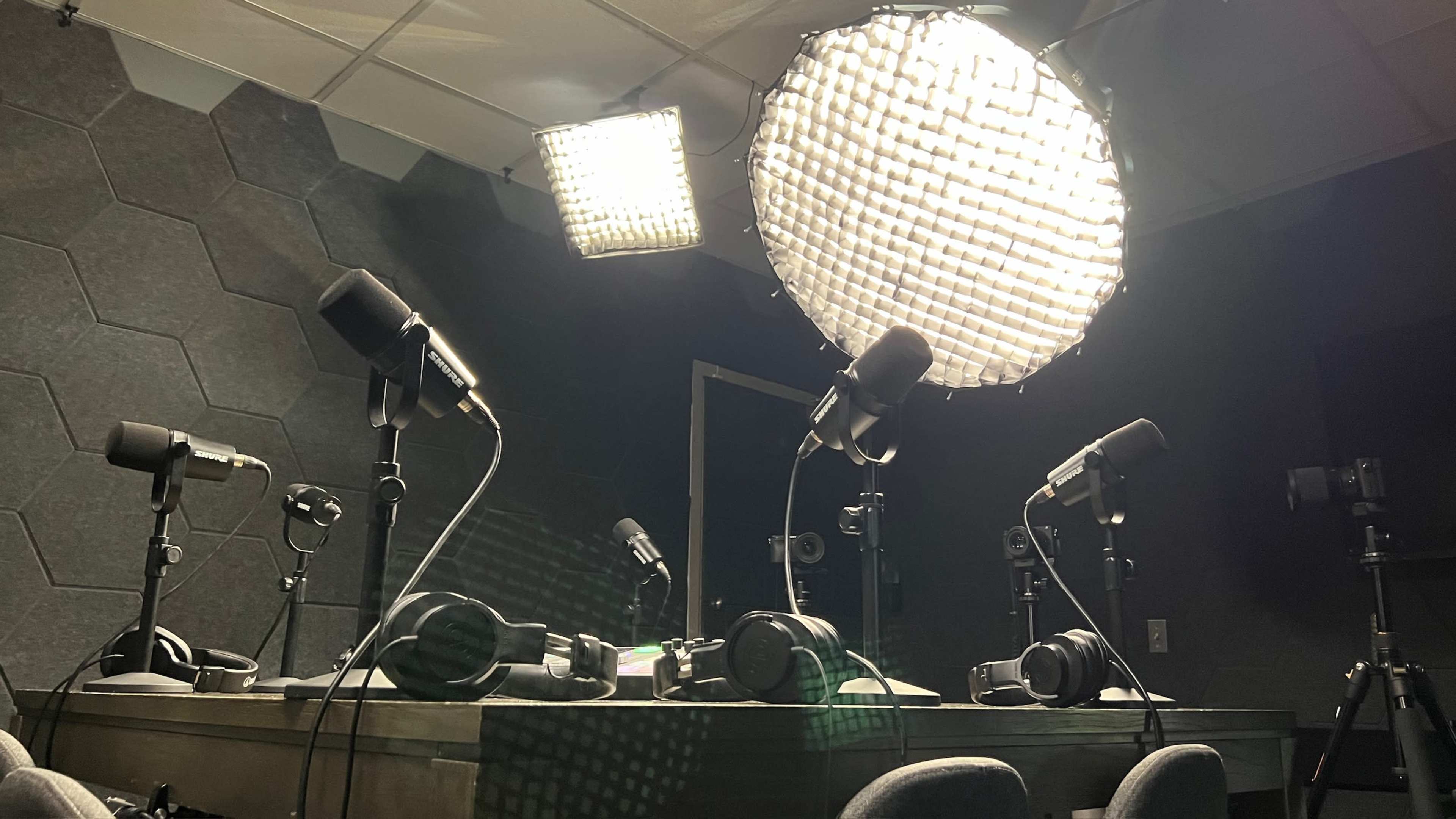 The image shows a recording studio with multiple microphones, headphones, and lights arranged on a table.