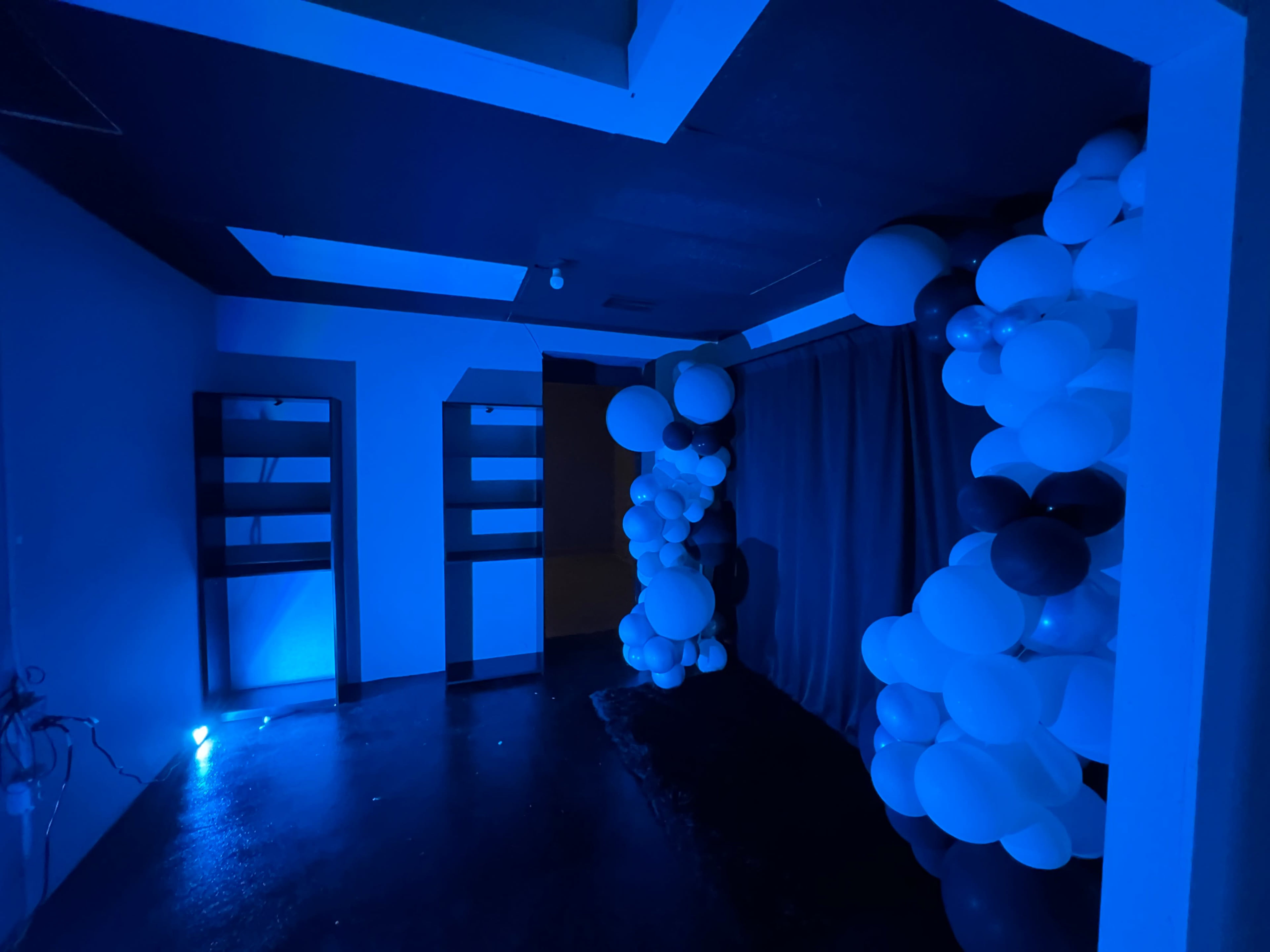 A dimly lit room with blue walls and decorations featuring clusters of white and dark balloons against a blue backdrop.