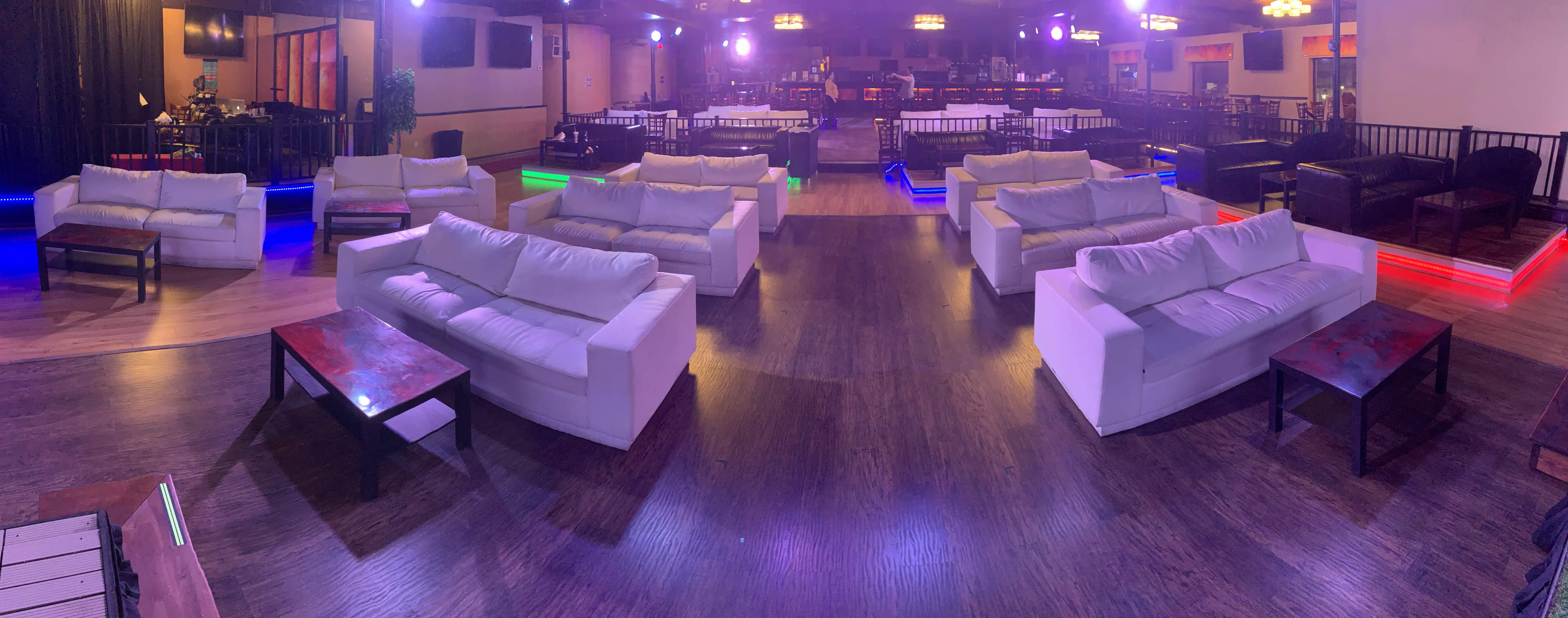 A spacious lounge area with white couches arranged around low tables, illuminated by colorful lights.