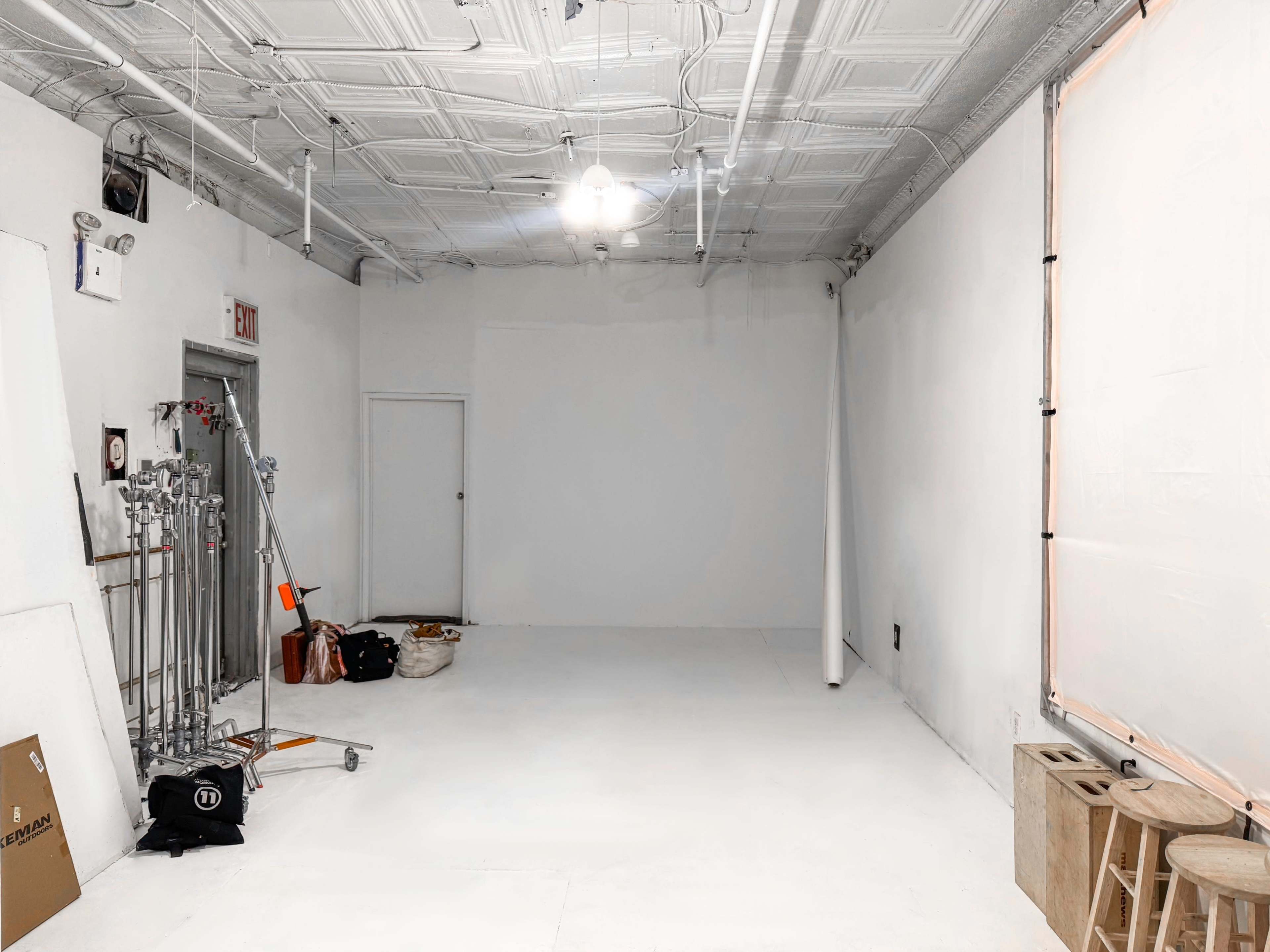 The image shows an empty room with white walls, a painted ceiling, and various equipment and materials stacked in one corner.