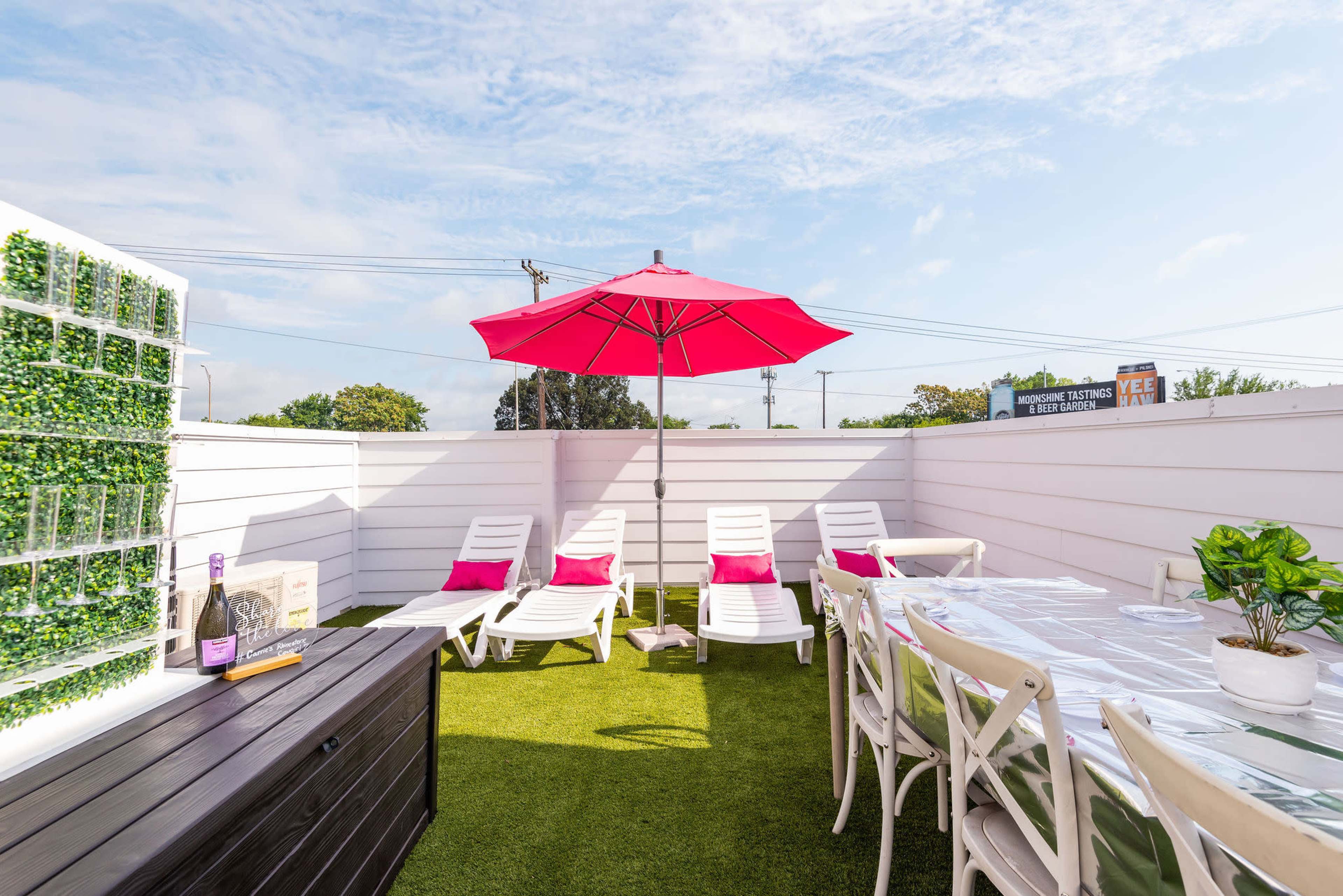 The image shows a rooftop patio with white furniture, green grass, a large red umbrella, and a table set for dining.