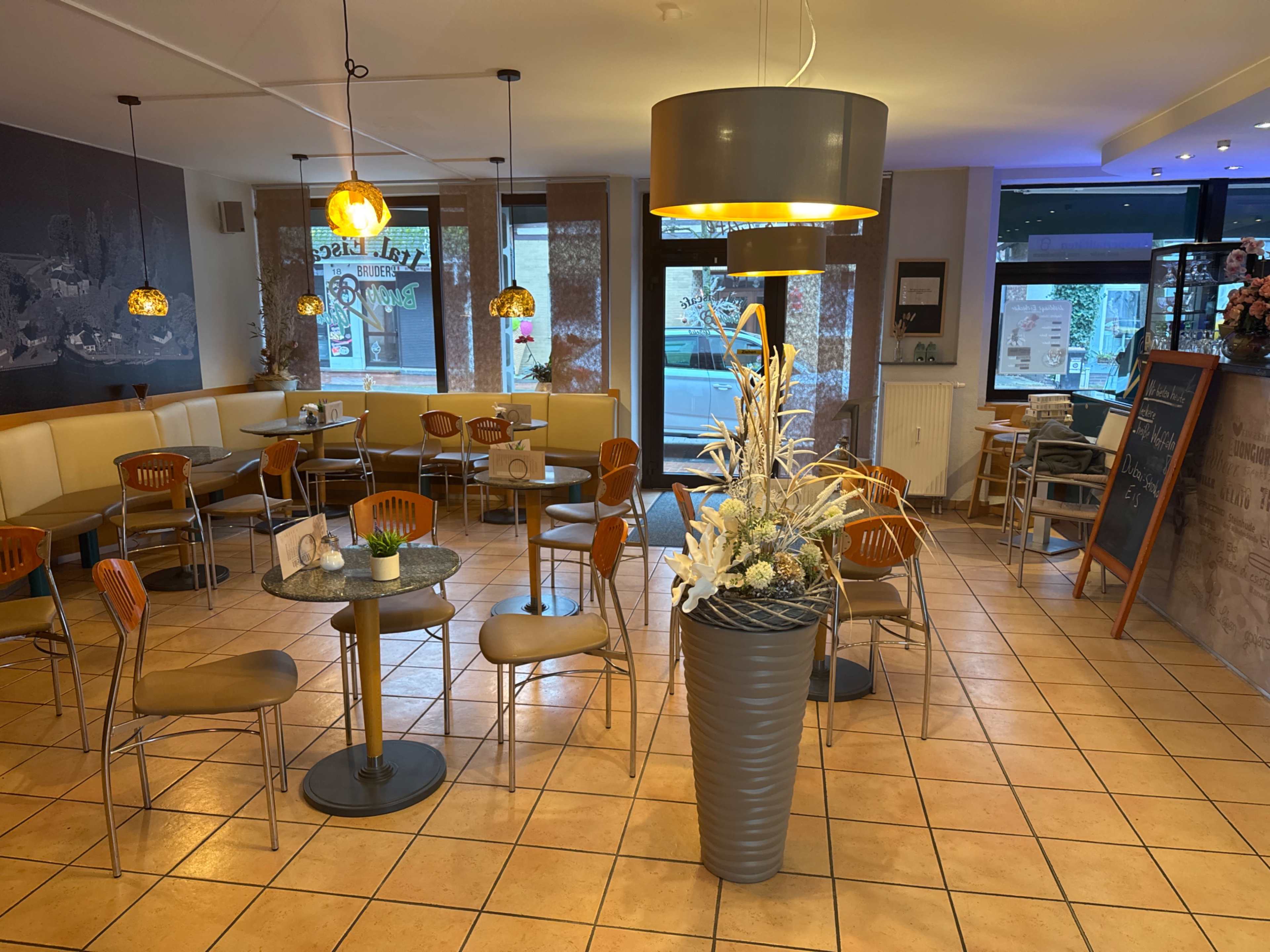 The image shows a cafe interior with multiple tables and chairs arranged around a floral centerpiece.