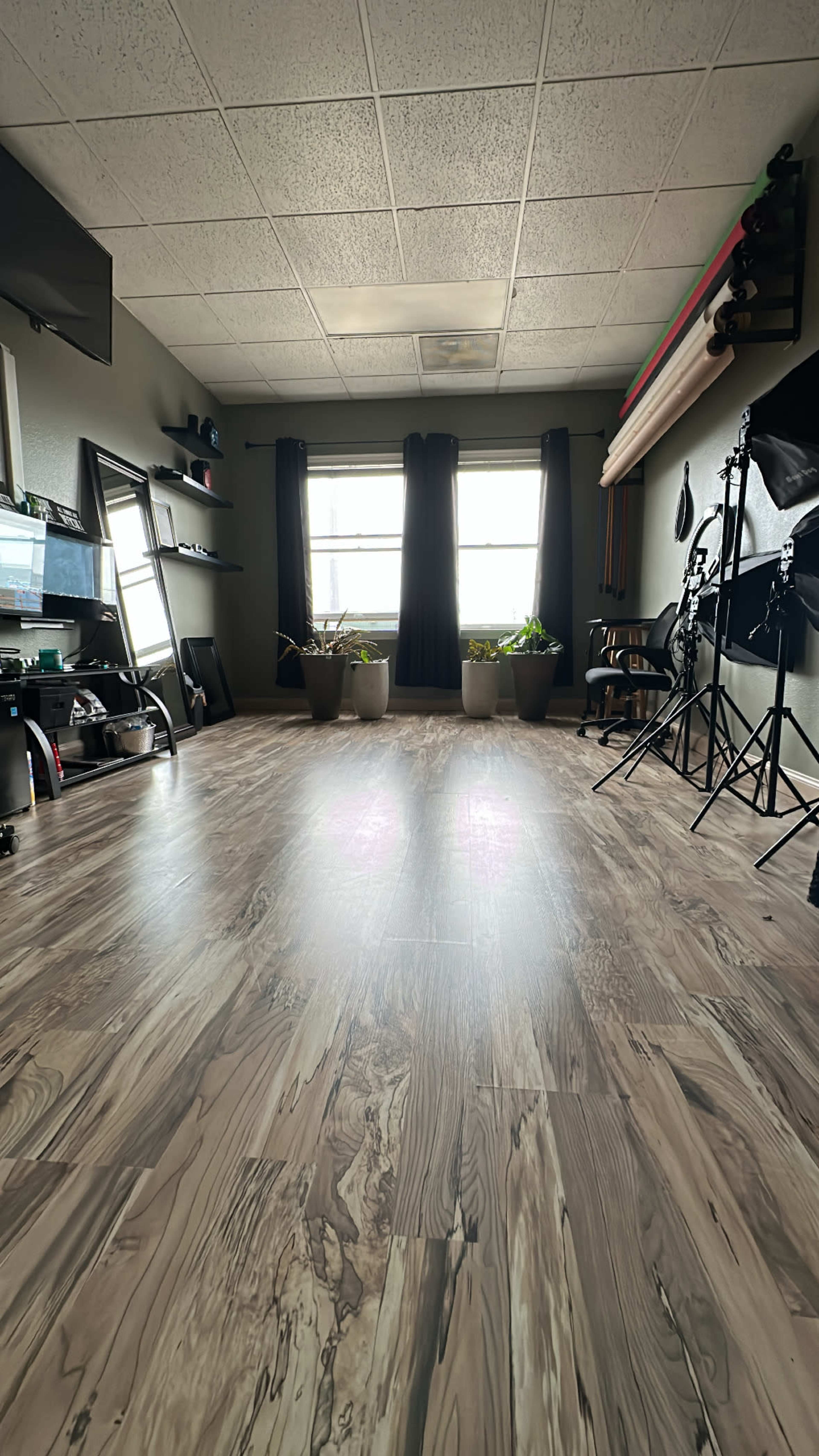 The image shows a spacious room with wooden floors, large windows, and various photography equipment along one side.