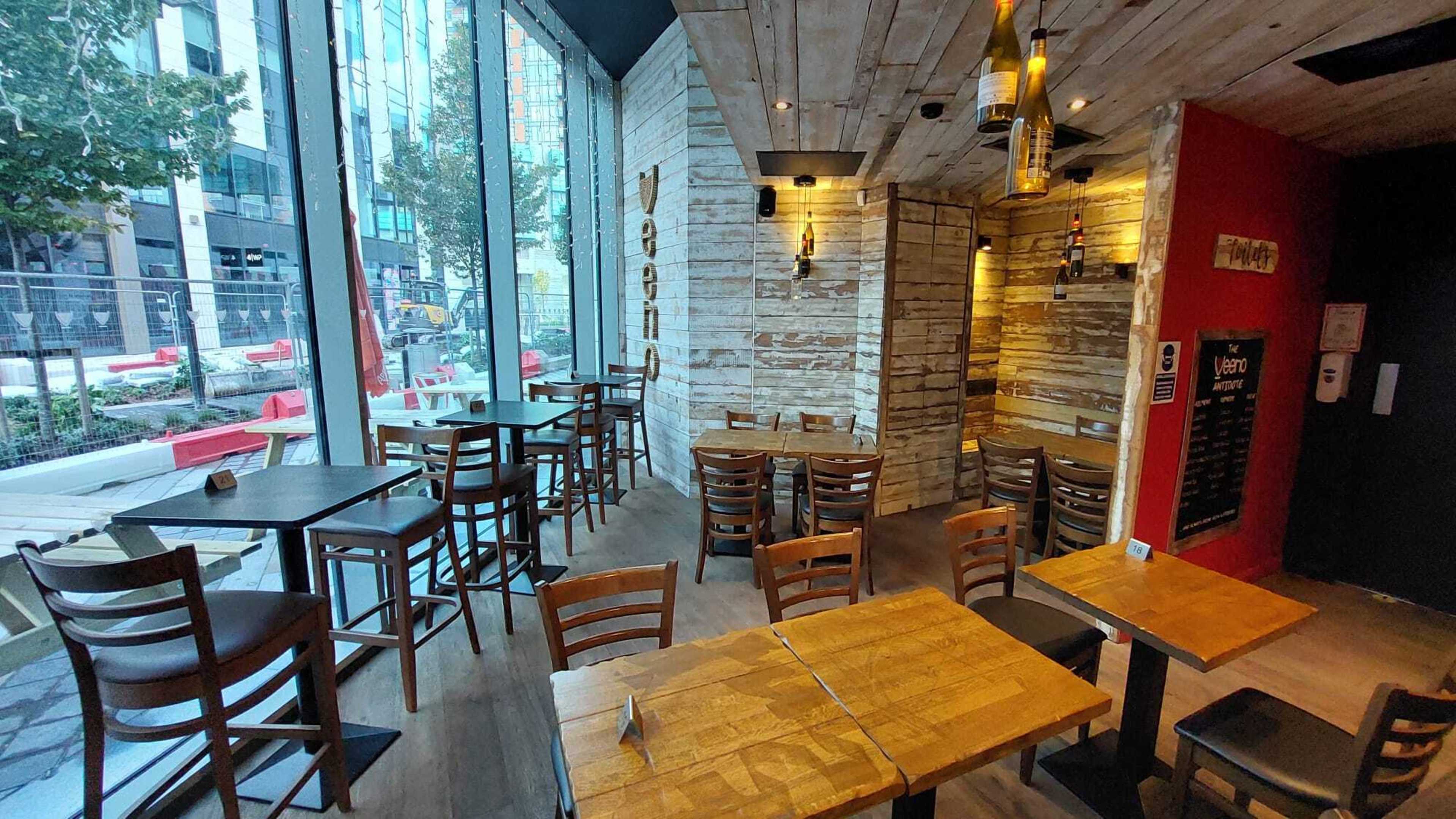 The interior of a restaurant featuring wooden tables and chairs, with large windows allowing natural light to illuminate the space.