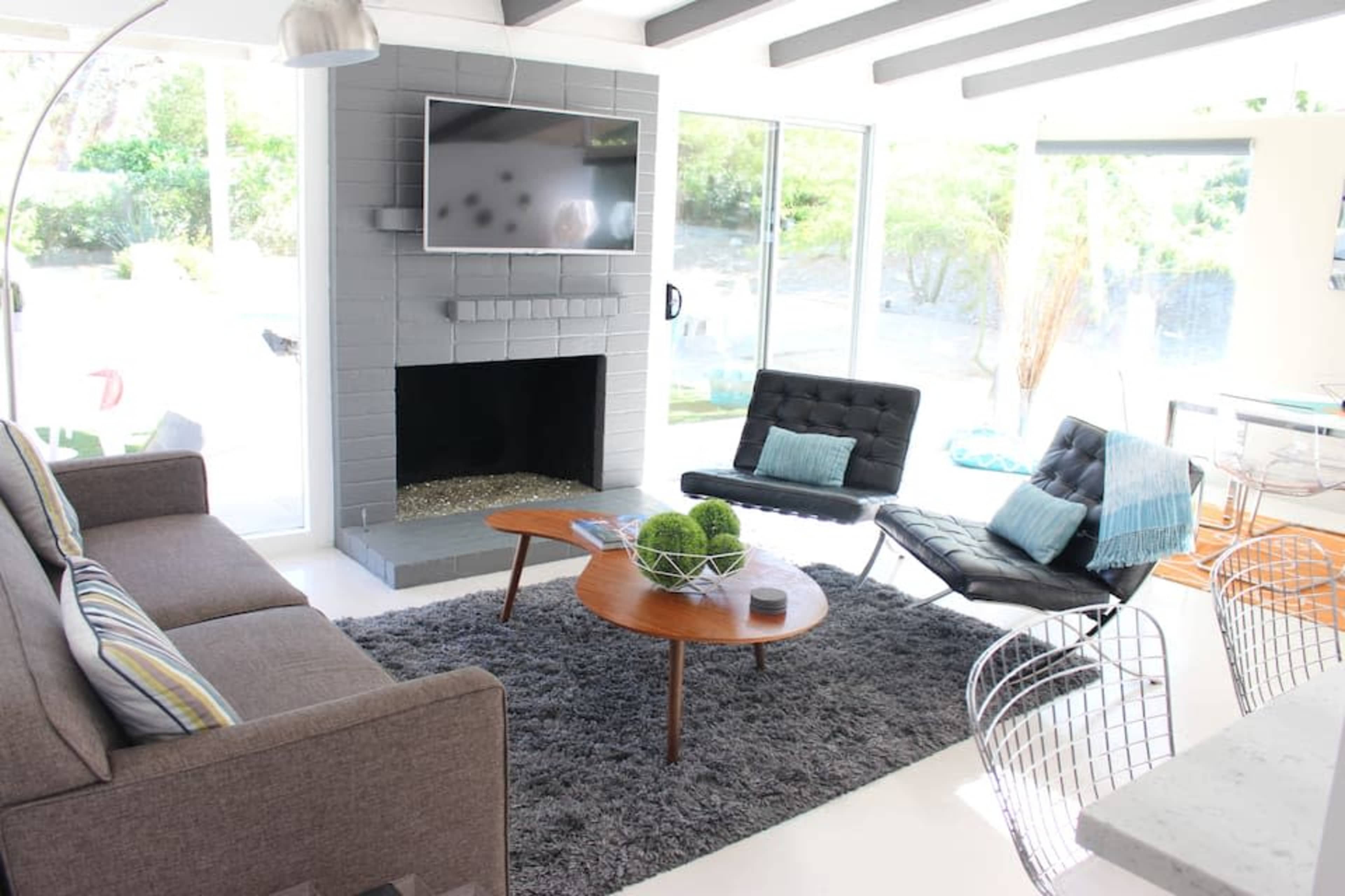 A modern living room features a gray fireplace, a flat-screen TV mounted on the wall, a comfortable sofa, and two distinctive chairs around a coffee table, all set on a plush area rug.