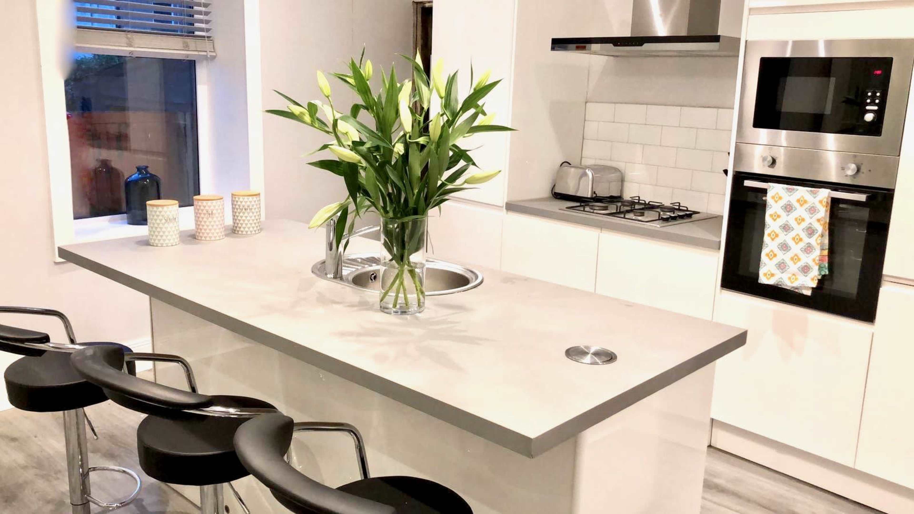 A modern kitchen features a central island with a vase of lilies and bar stools along one side.