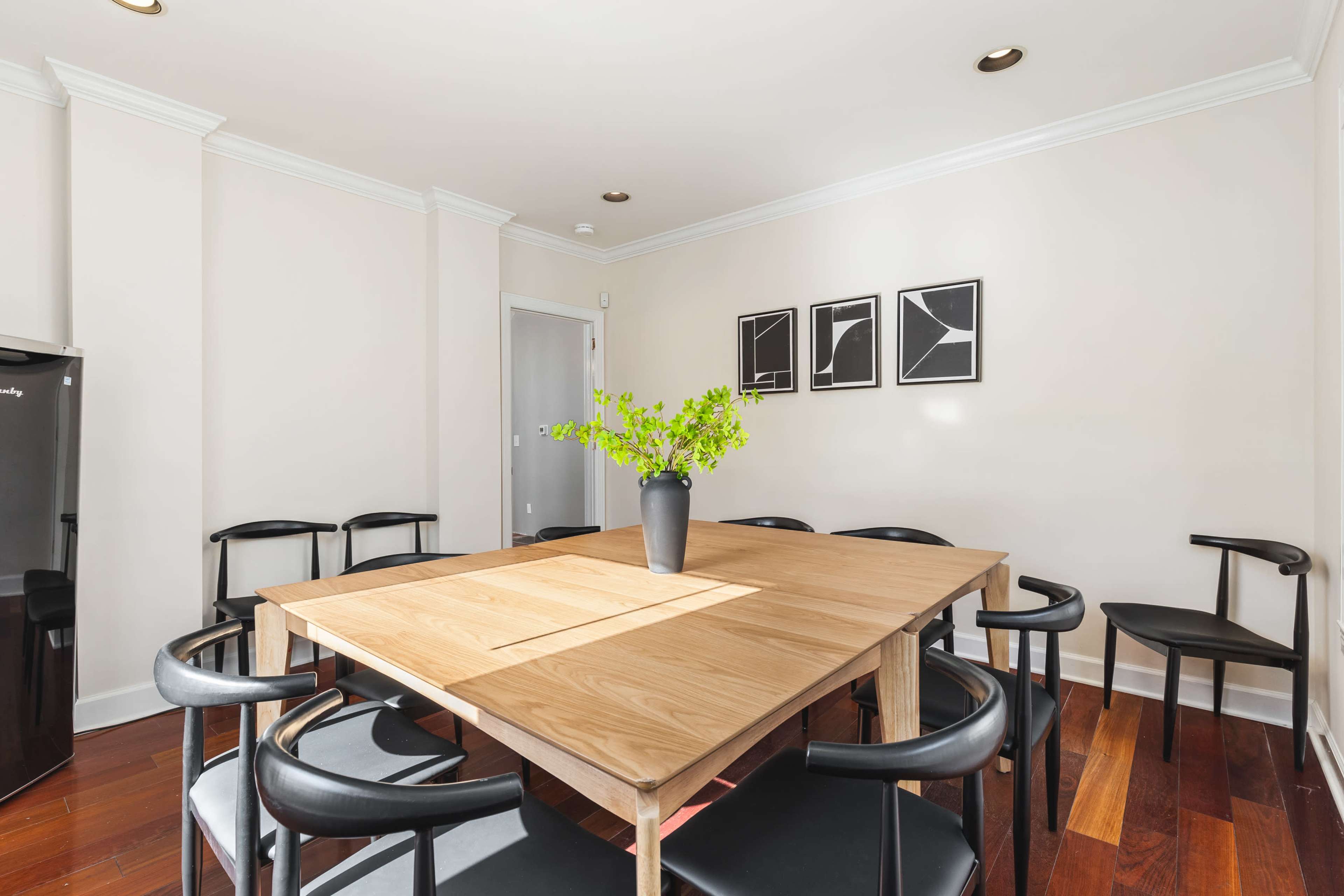 A dining area features a wooden table surrounded by black chairs, with a small vase of greenery in the center.