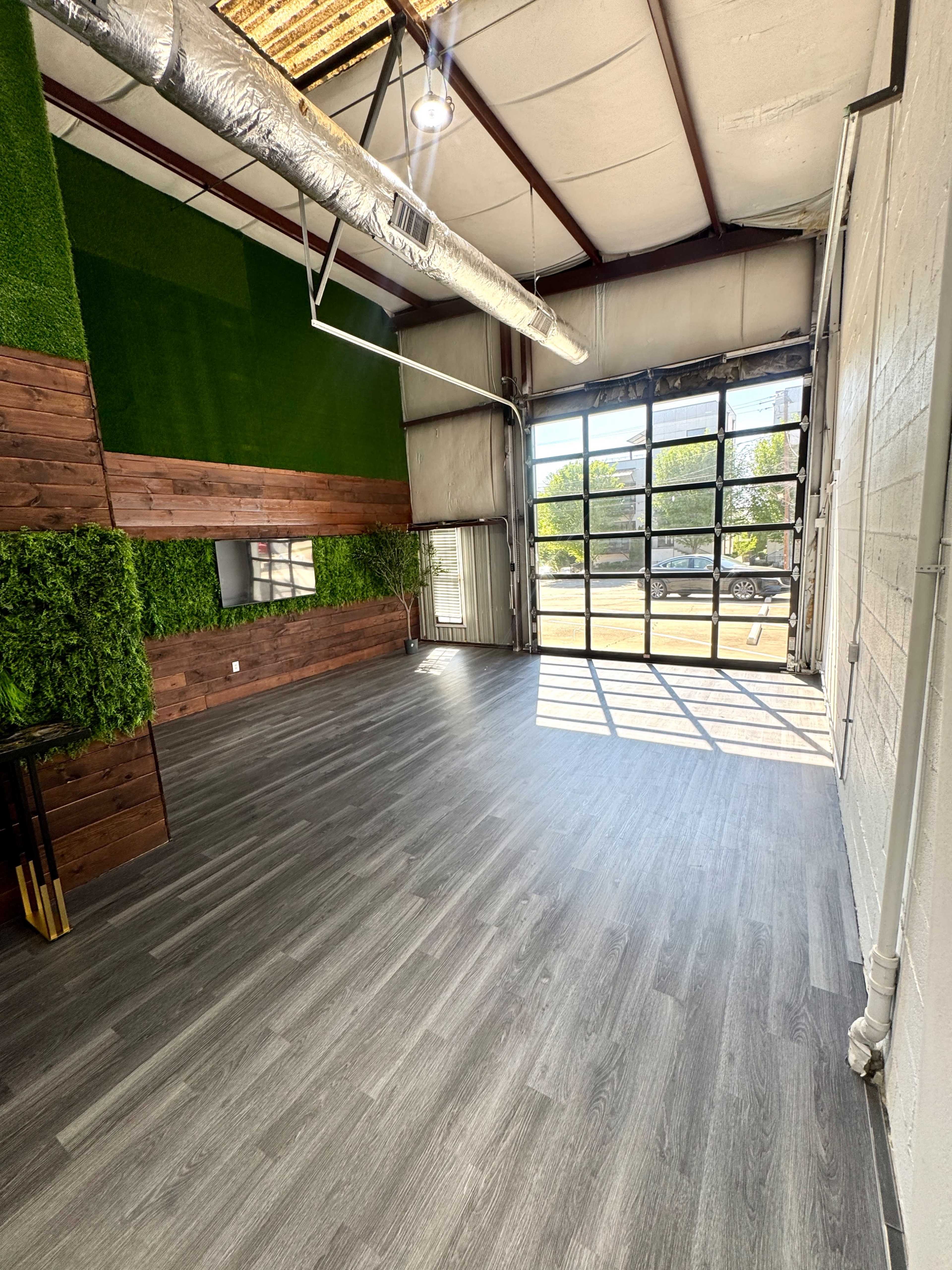 The image shows an empty interior space with wooden accents, green wall panels, large windows, and a polished floor.