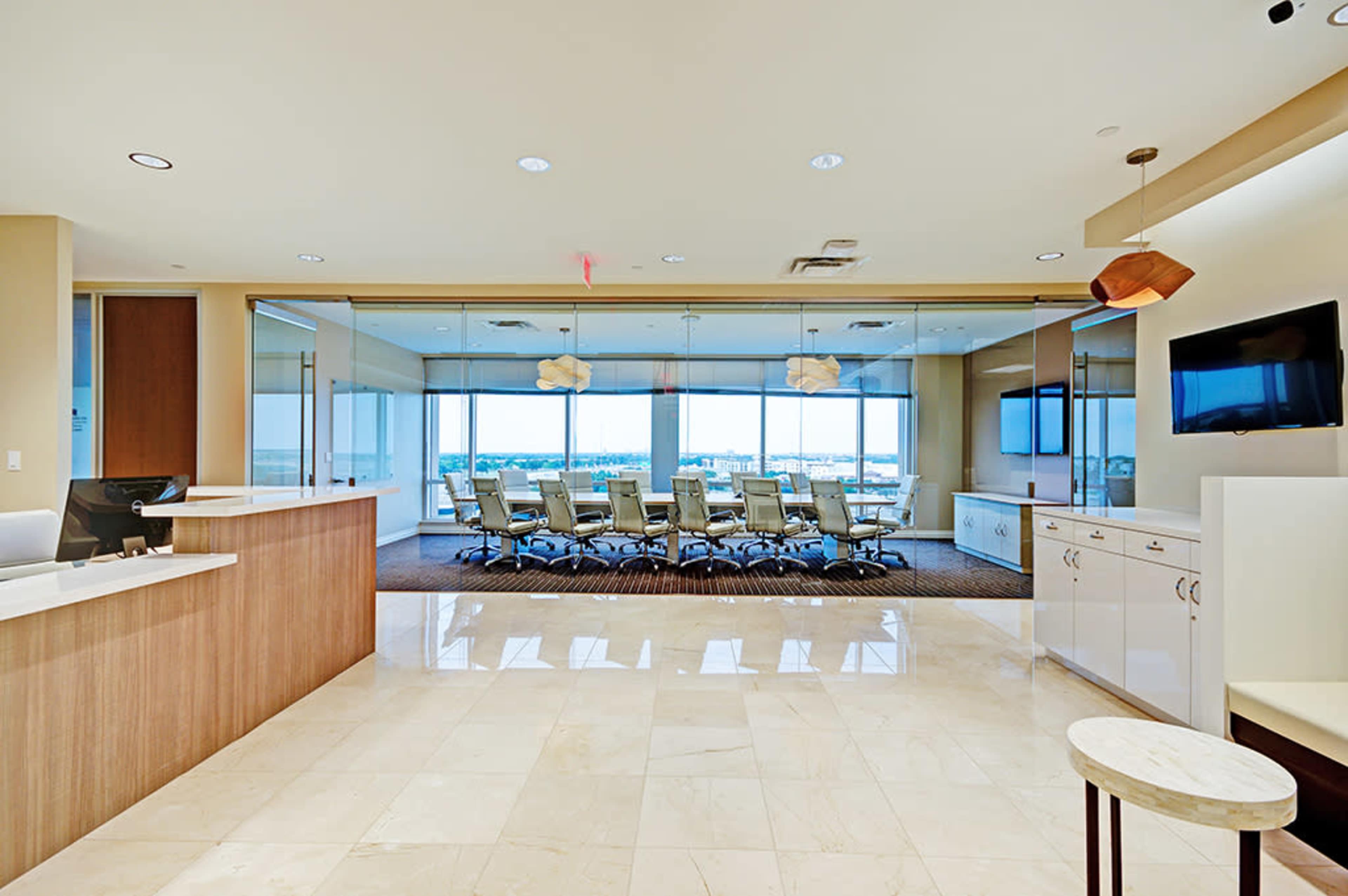 A modern office reception area leading to a conference room with large windows and a long table surrounded by chairs.