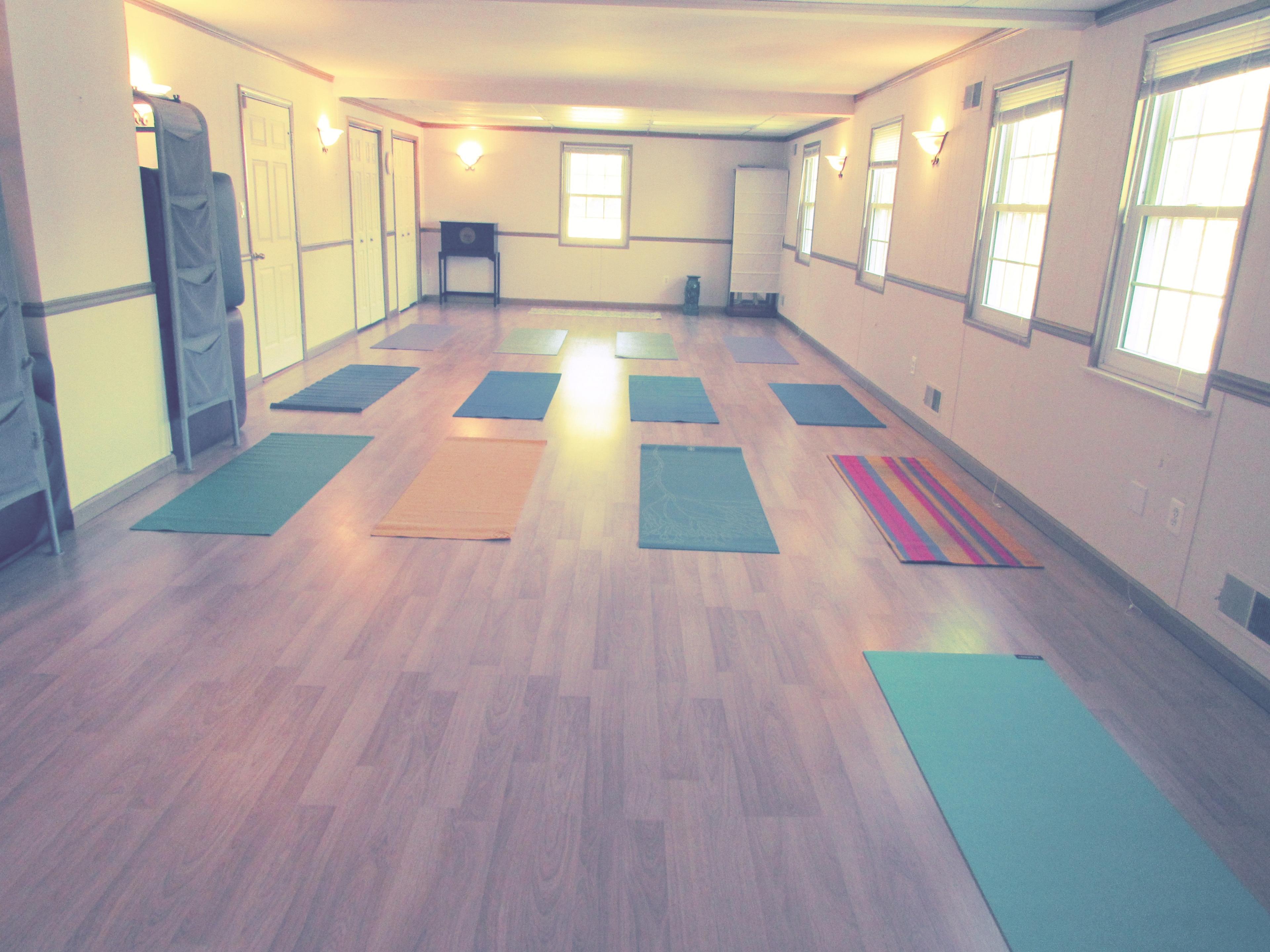 A spacious room with wooden flooring and multiple yoga mats arranged in a grid pattern.