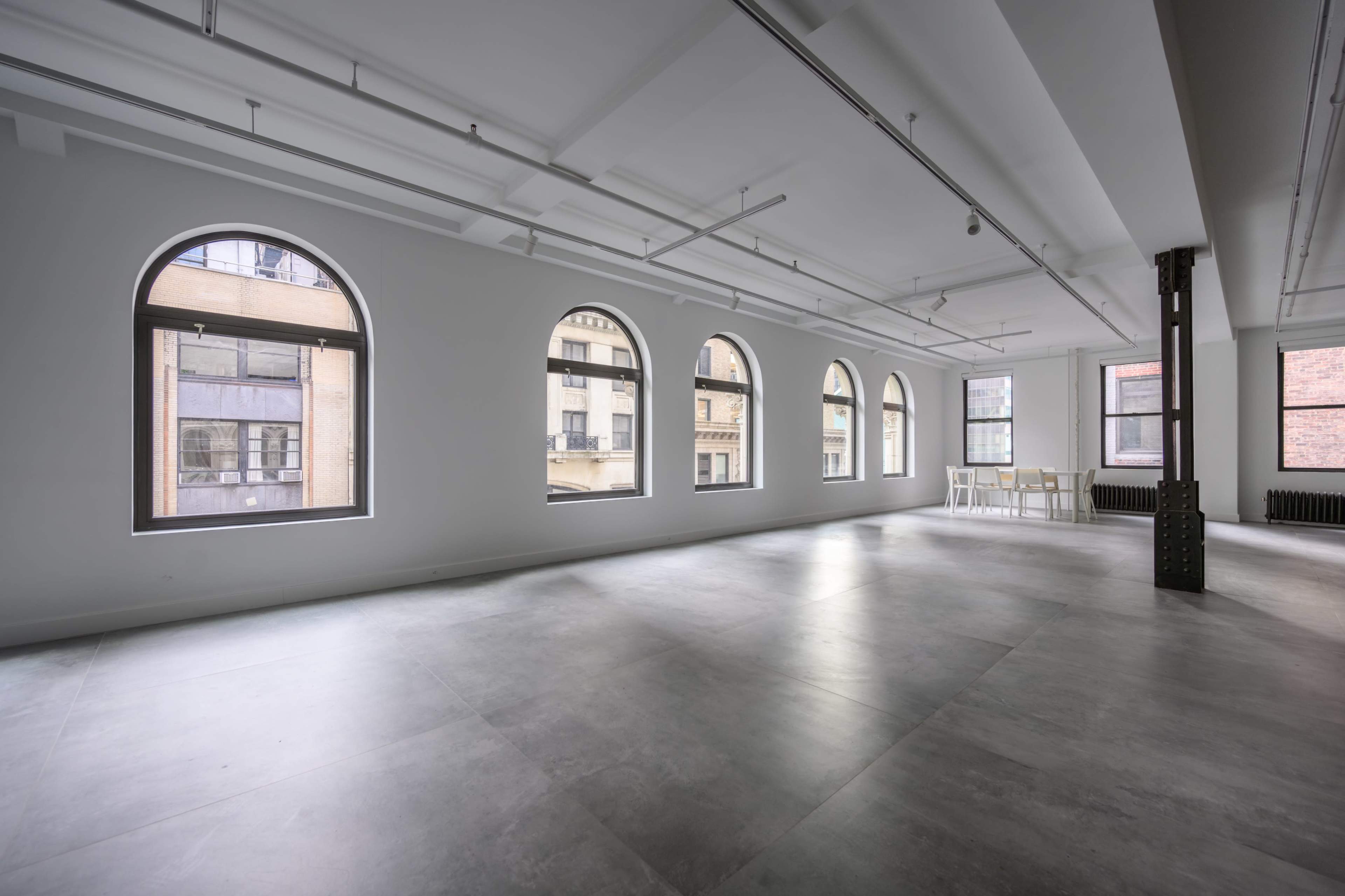 The image shows a spacious, empty room with large arched windows and concrete flooring.