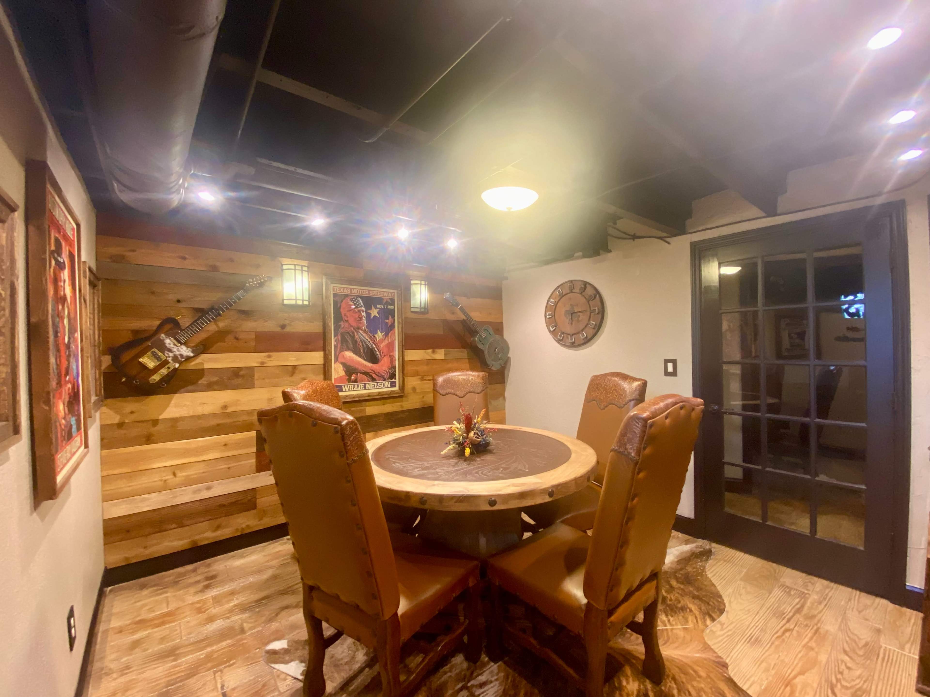 A sunlit dining room featuring a round wooden table surrounded by brown leather chairs, with wooden paneling and decorative items on the walls.