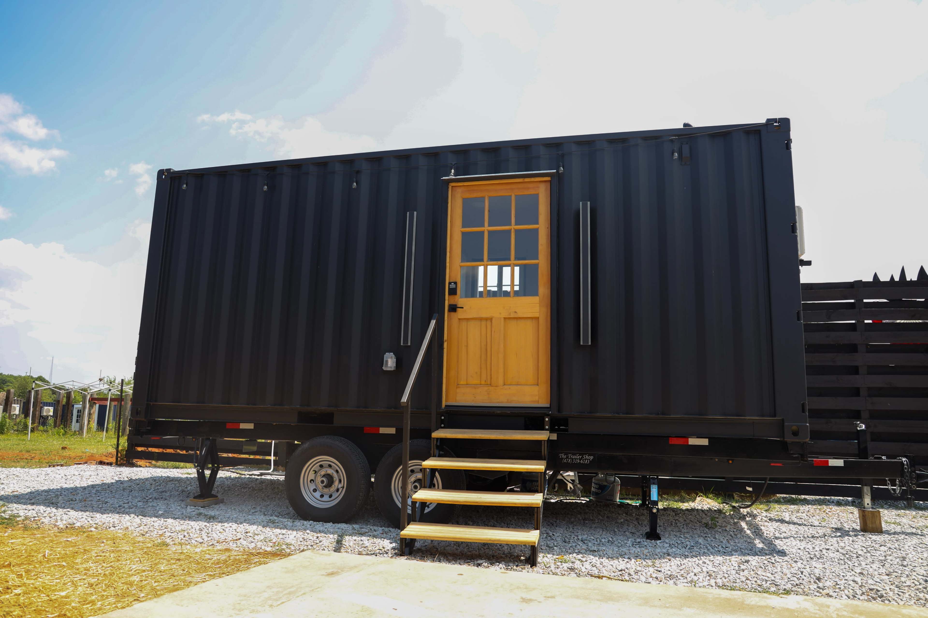 A black shipping container converted into a portable structure with a wooden door and steps leading up to it.