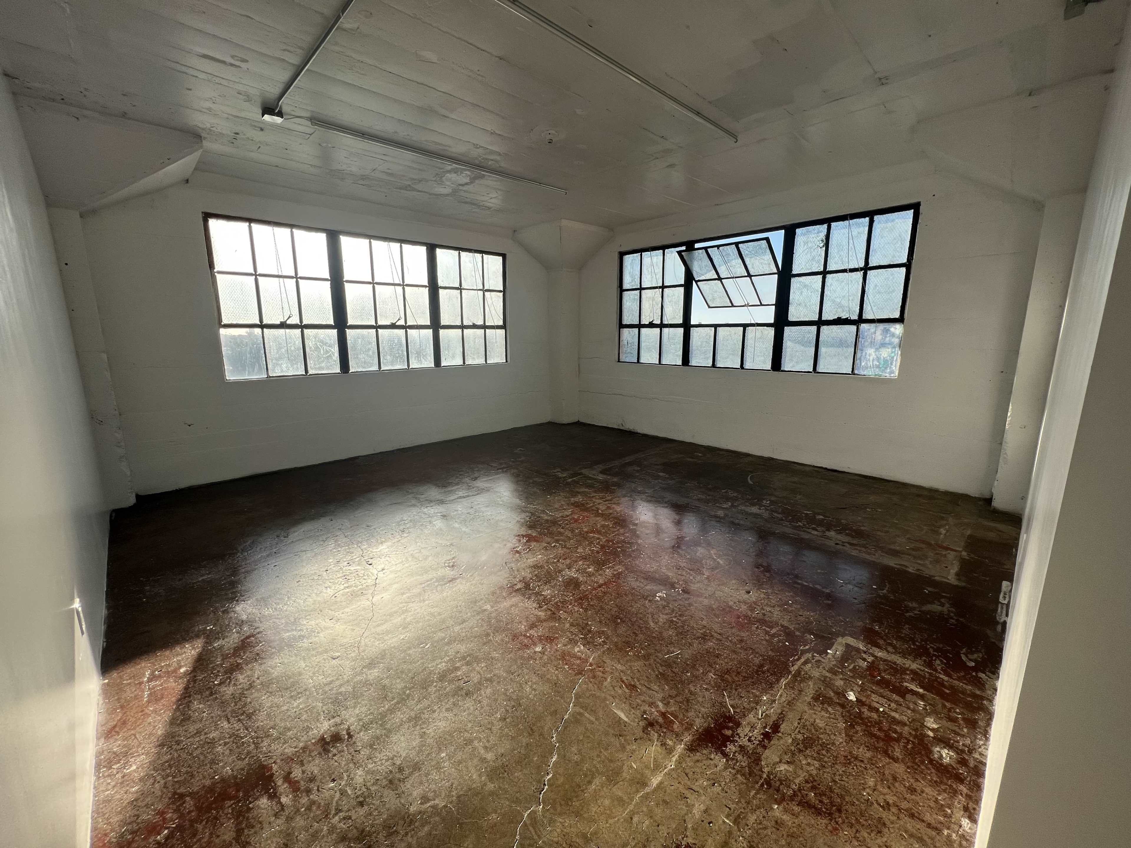 An empty room with large windows, a concrete floor, and white walls.