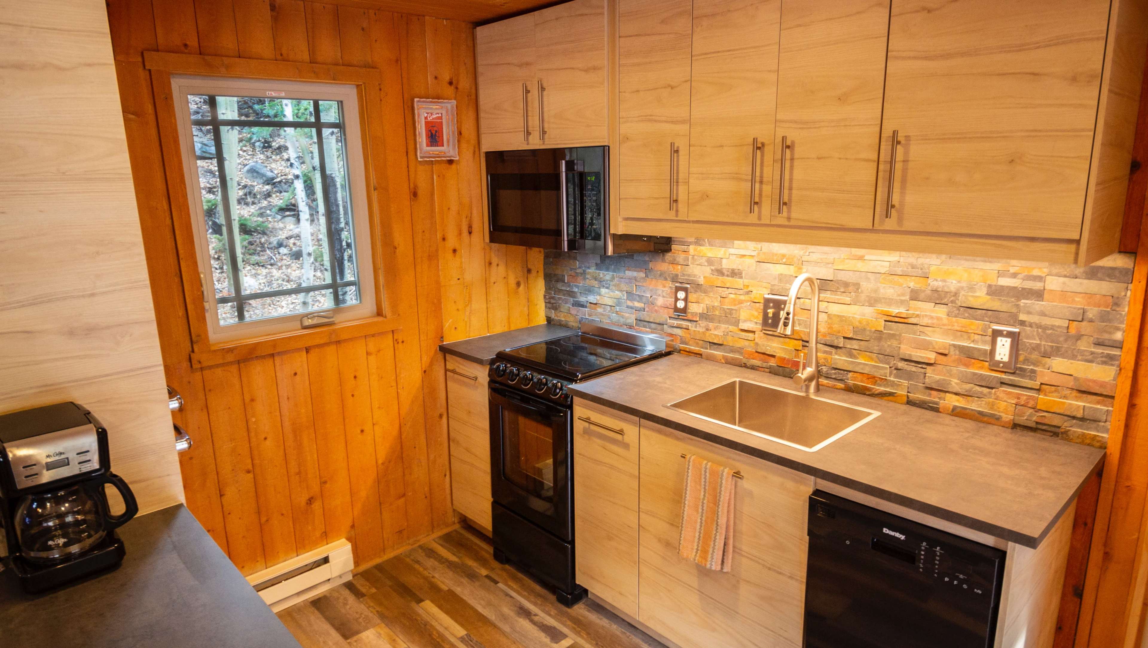 The image shows a modern kitchen featuring wooden walls, a countertop, and appliances including a stove, microwave, and coffee maker.