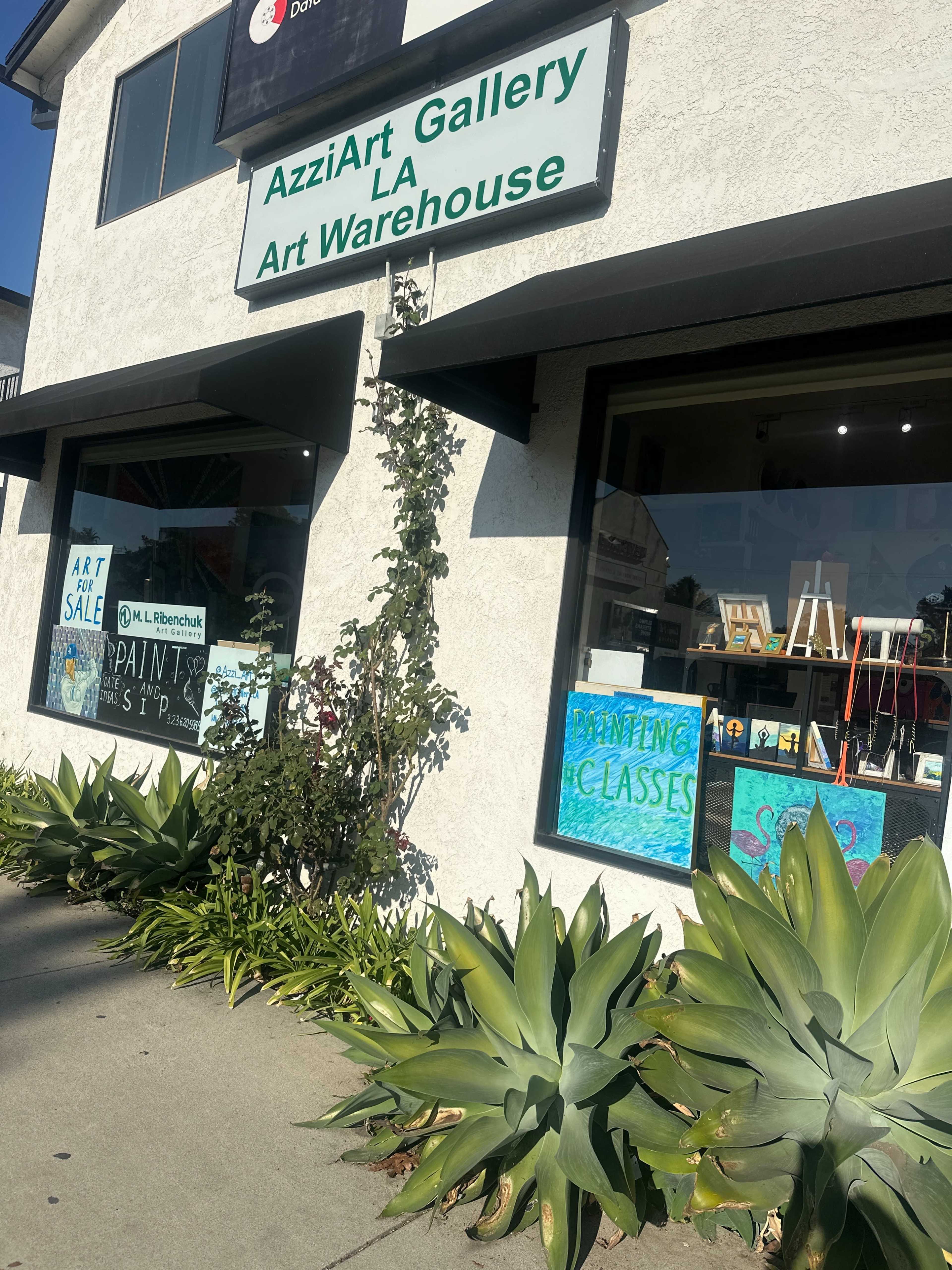 The image shows the exterior of AzziArt Gallery LA Art Warehouse, featuring a sign and colorful storefront windows displaying artwork and advertisements for classes.
