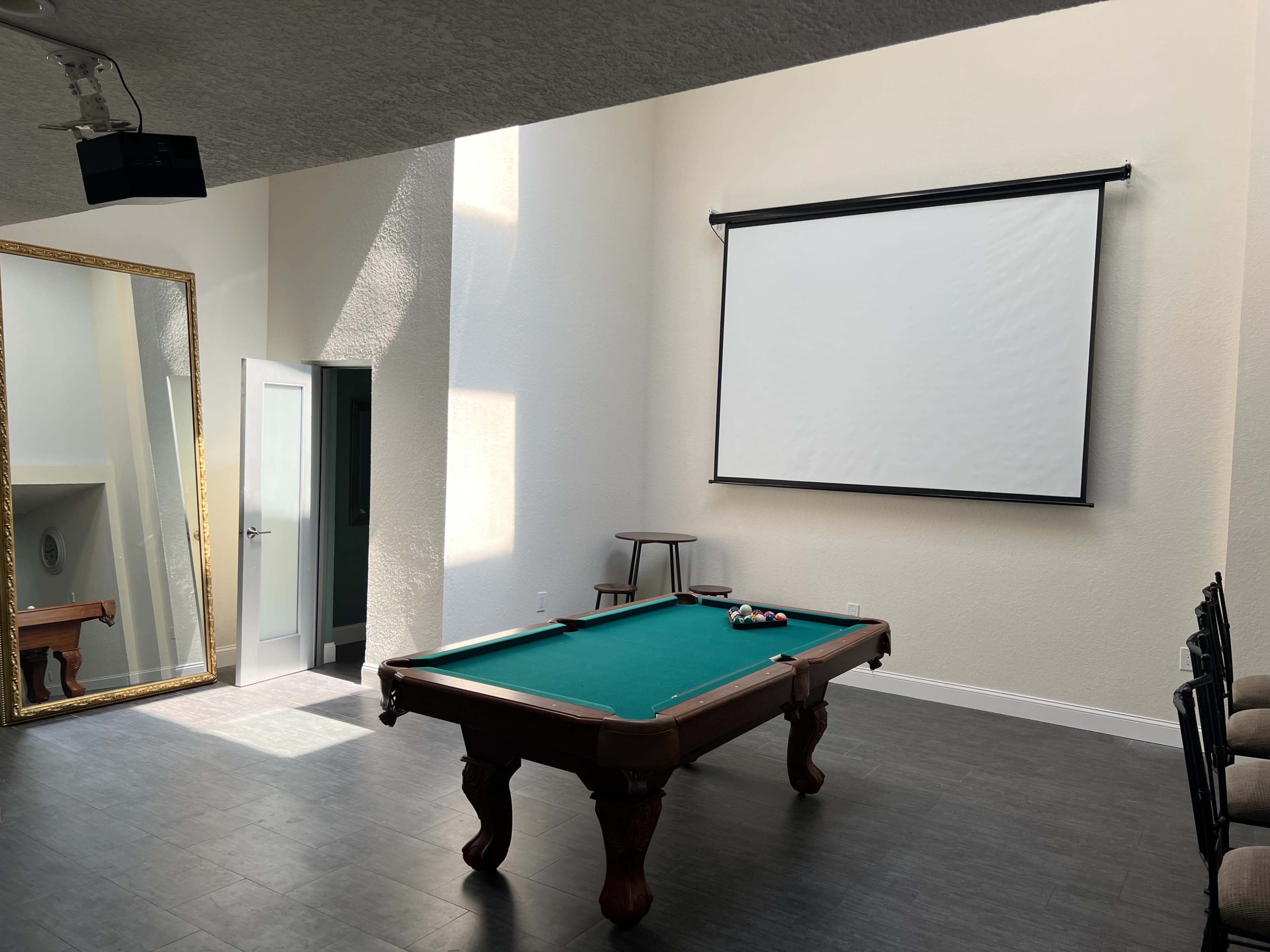 A bright room with a pool table, a large mirror, and a projection screen on the wall.