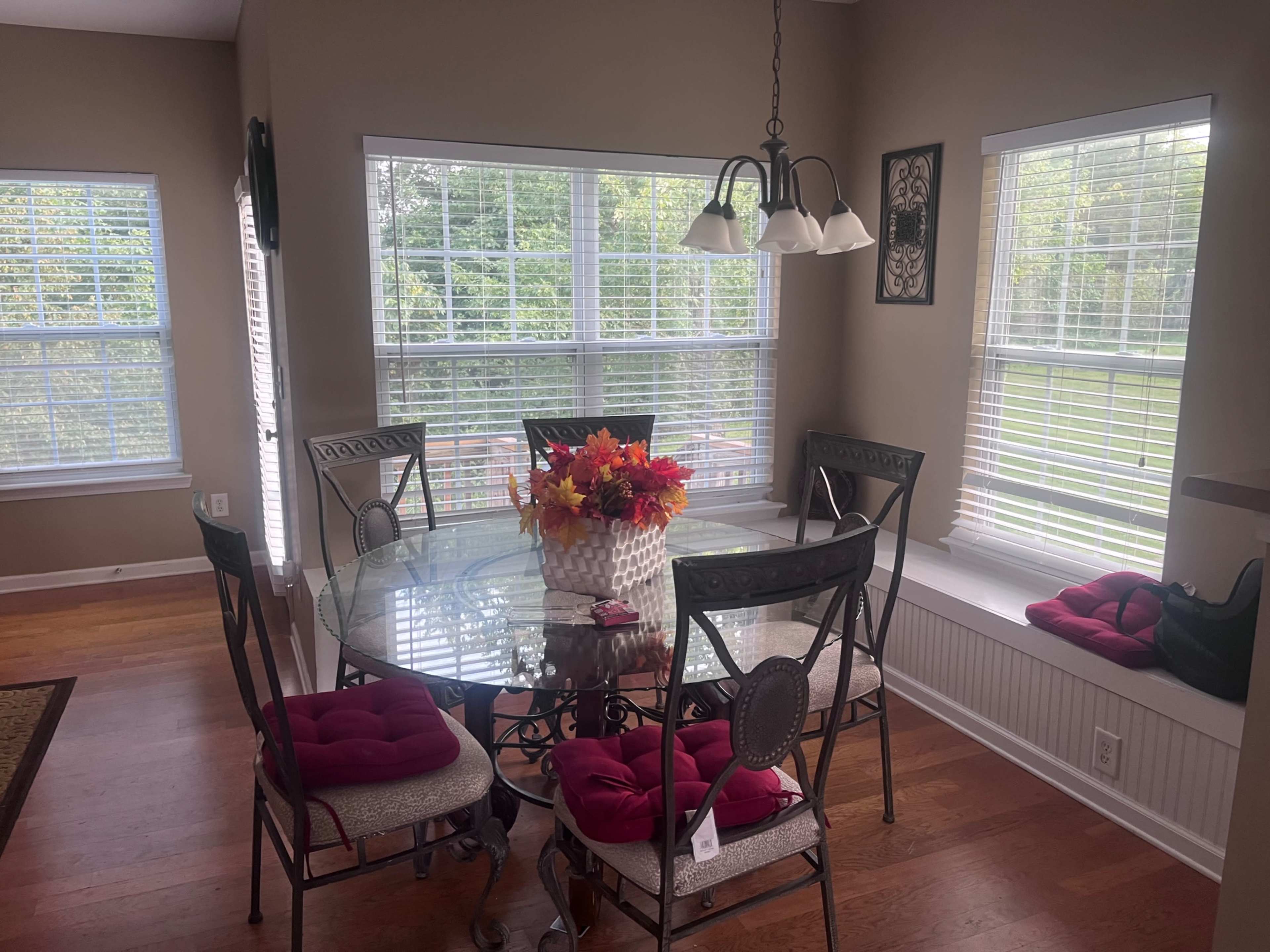A glass dining table surrounded by six chairs, with a centerpiece of colorful flowers, is positioned near large windows that allow natural light to flood the space.