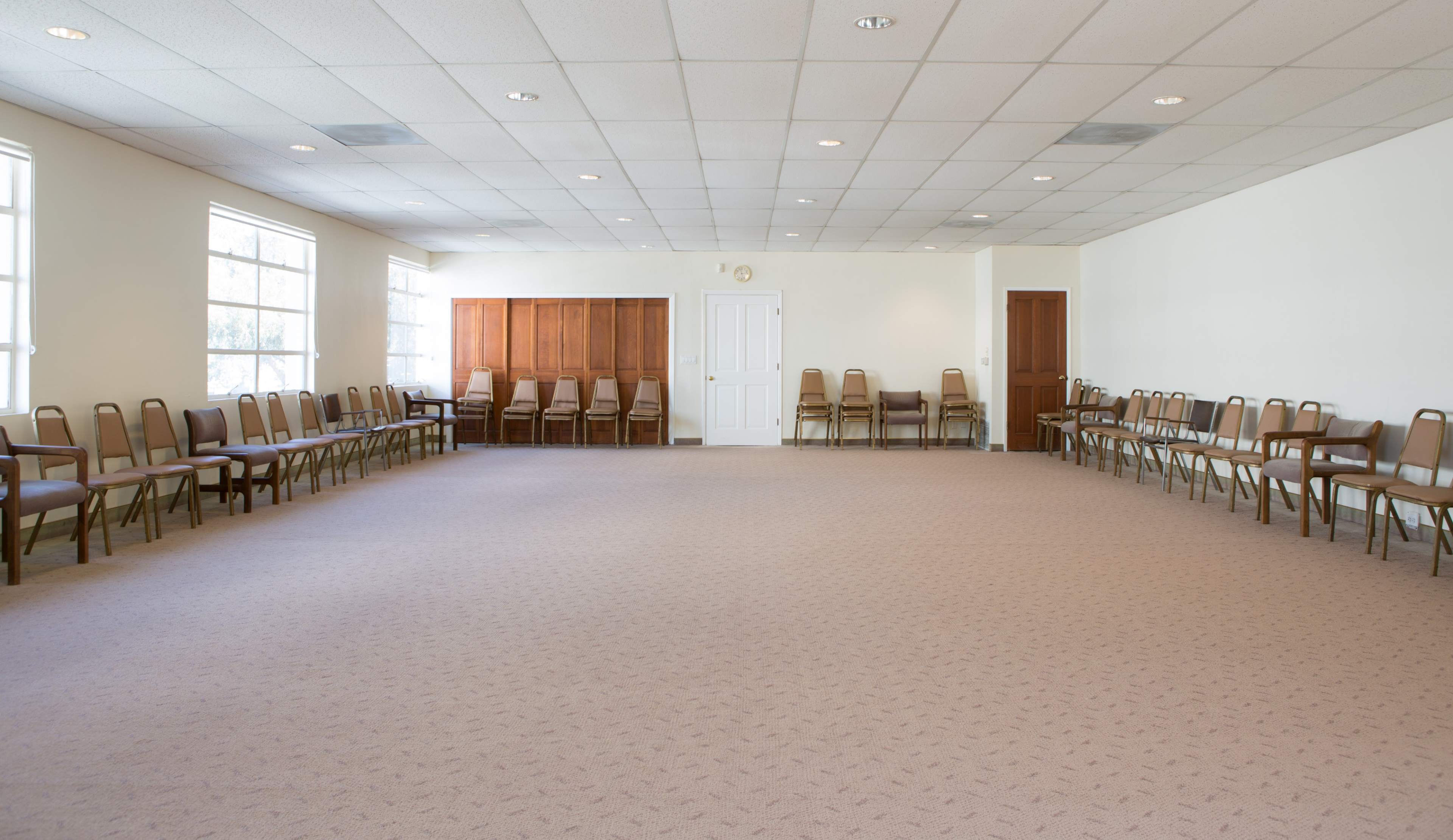 A spacious room with two rows of empty chairs along the walls and a wooden cabinet at the back.