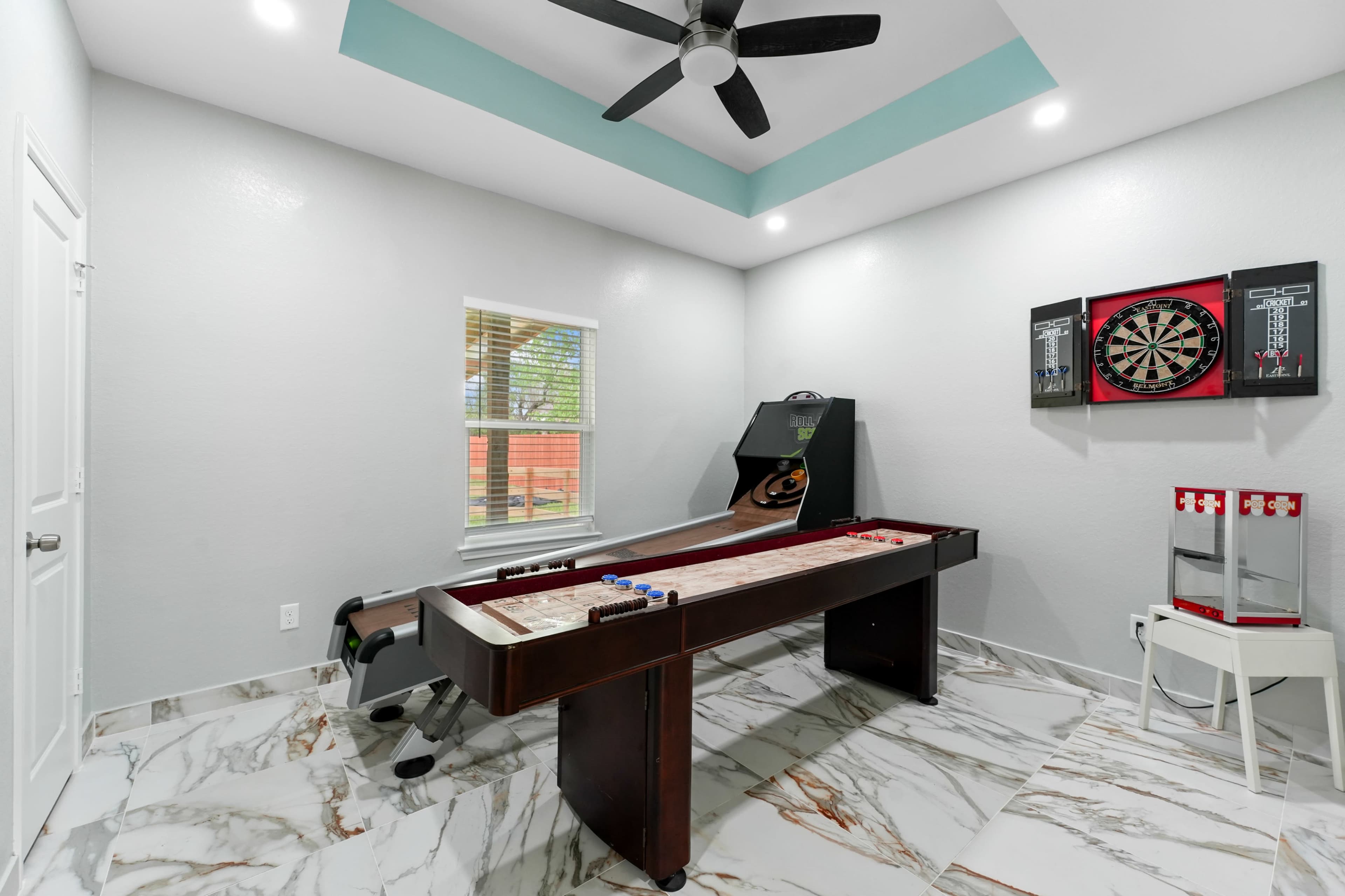 The room features a shuffleboard table, a dartboard, and a sleek, modern design with marble flooring and a ceiling fan.