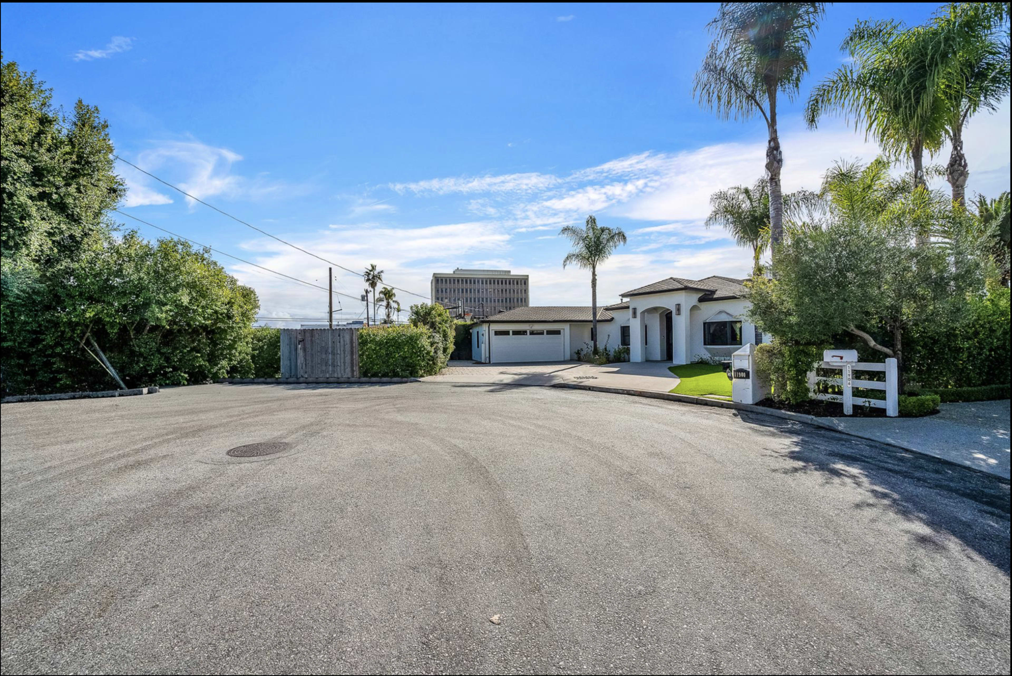 A residential street scene features a modern house with palm trees and a circular driveway.