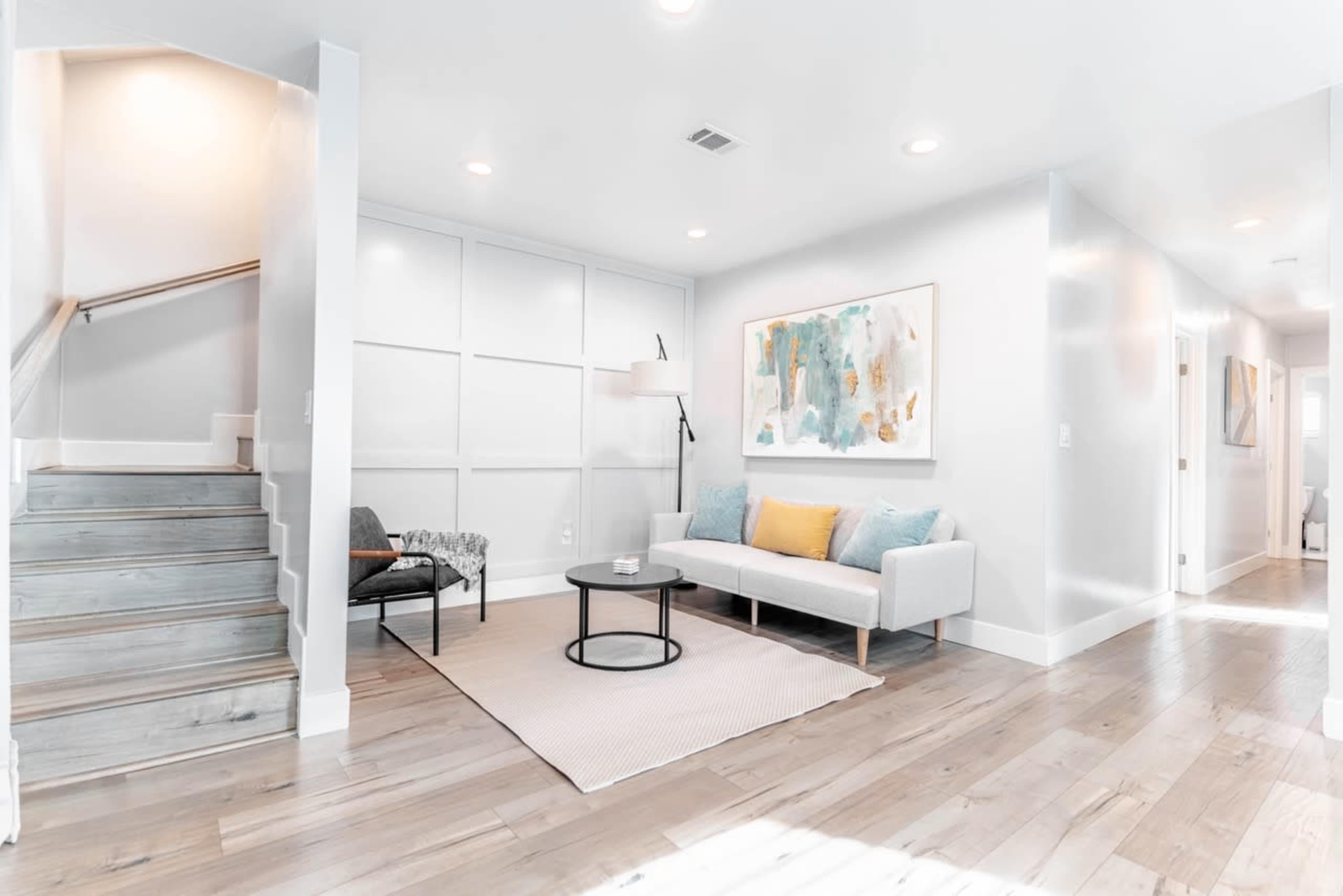 A bright, modern living room with a light gray sofa, a round black coffee table, and a large abstract painting on the wall.