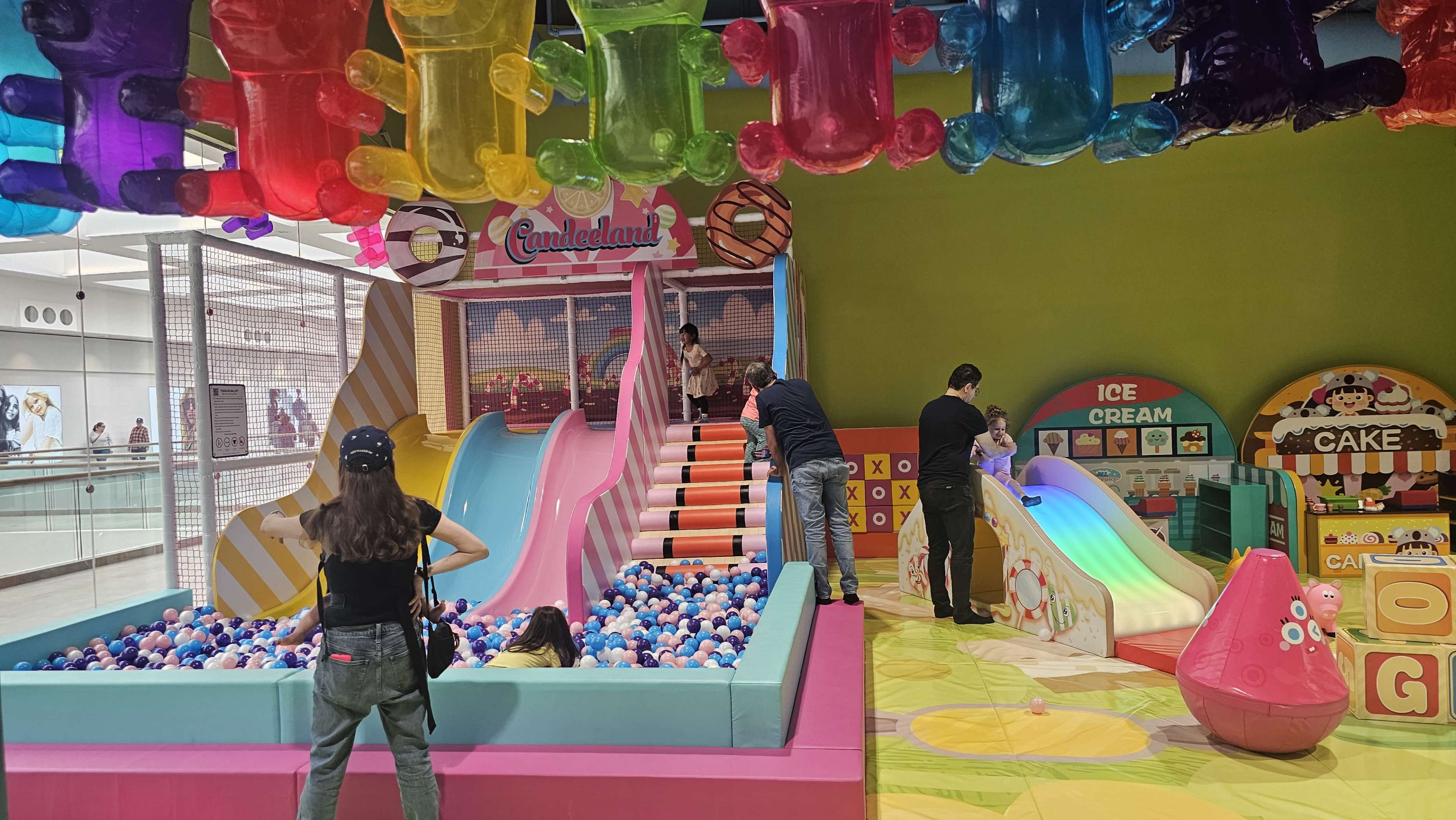 The image shows a colorful indoor play area with a ball pit, slides, and various play structures for children.