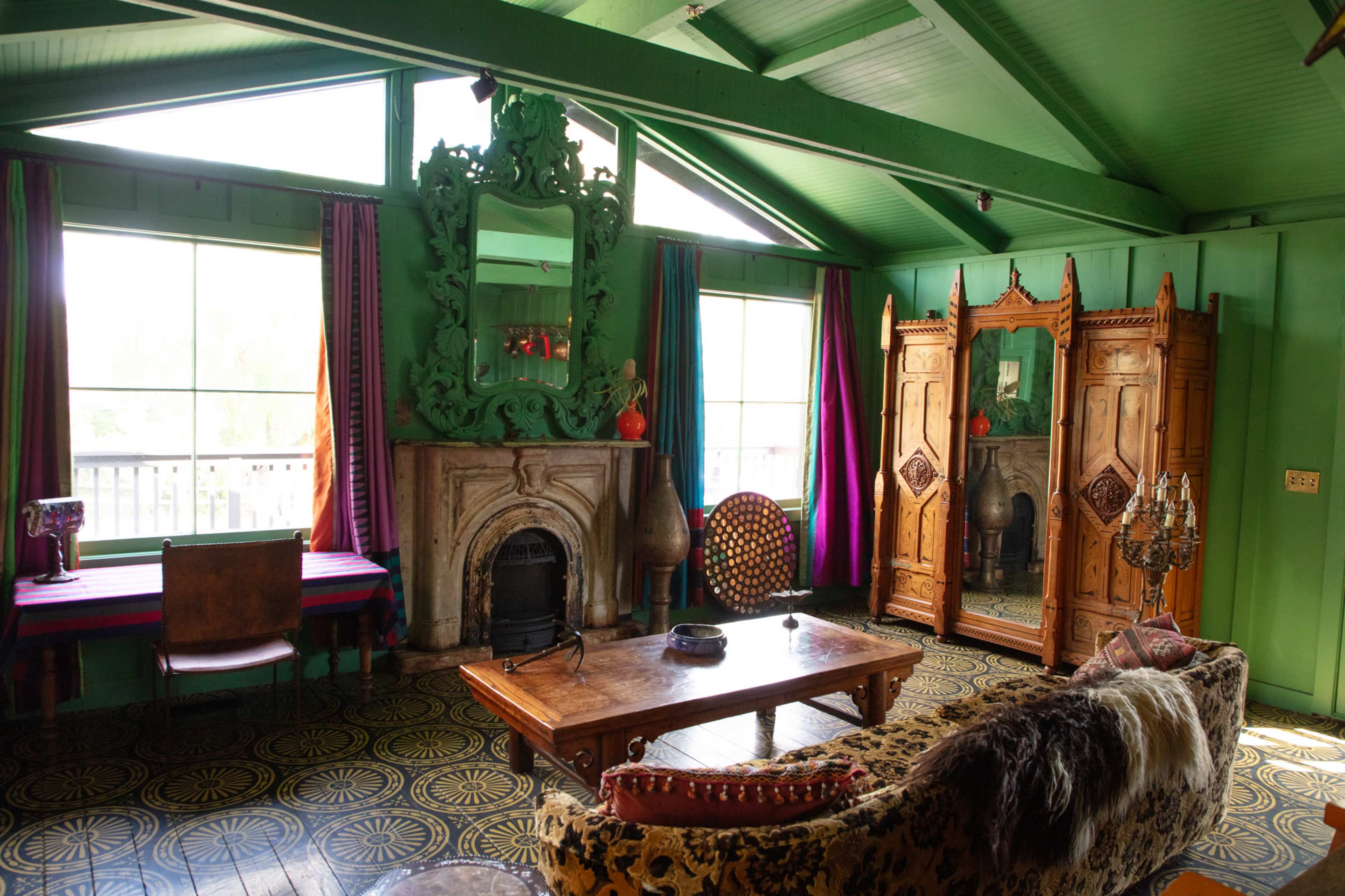 The interior features vivid green walls, large windows, a wooden table, and a mix of vintage furniture, including a plush sofa and ornate cabinetry.