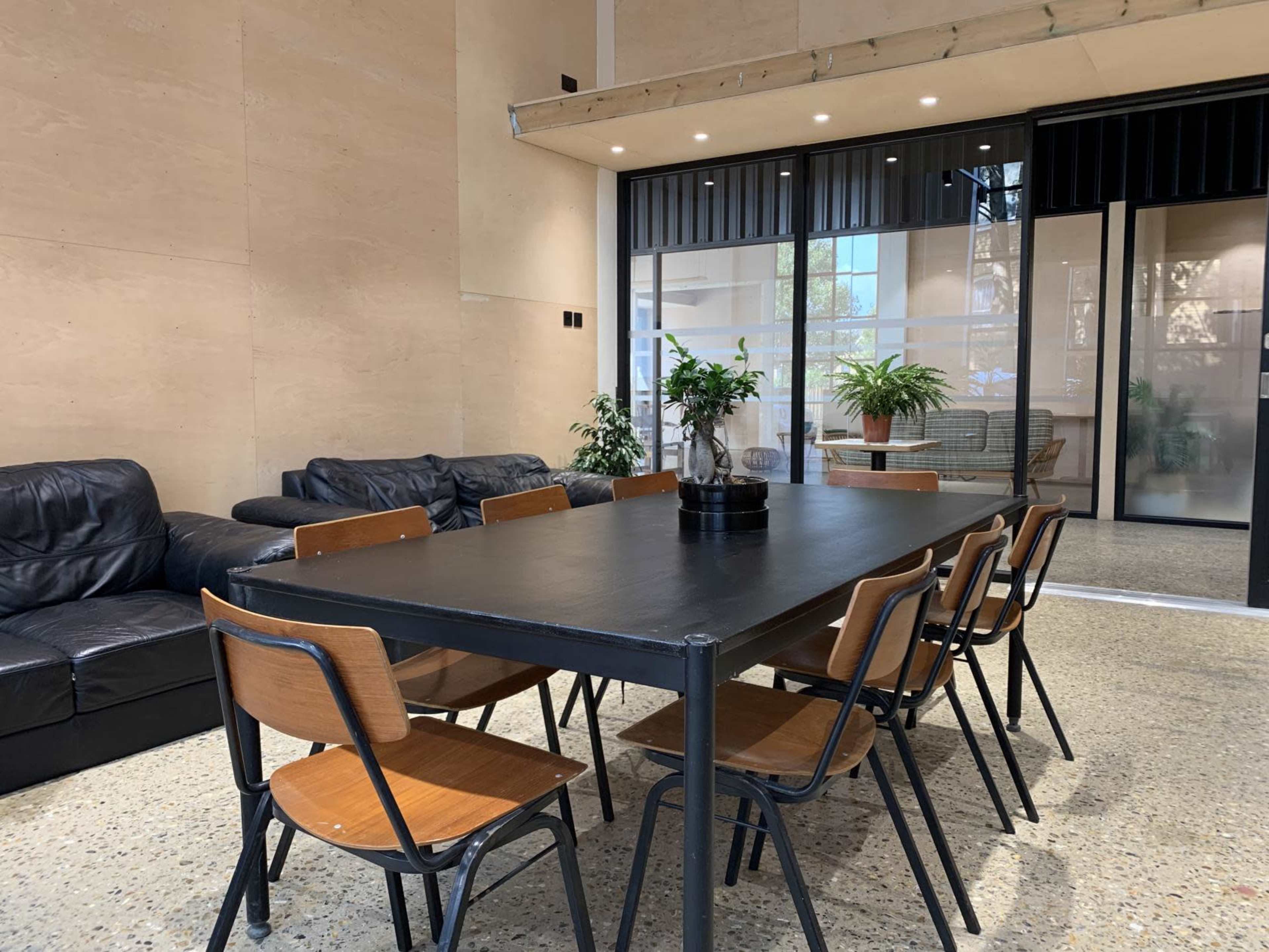 A modern meeting room with a long black table surrounded by wooden chairs, and a couch area in the background.