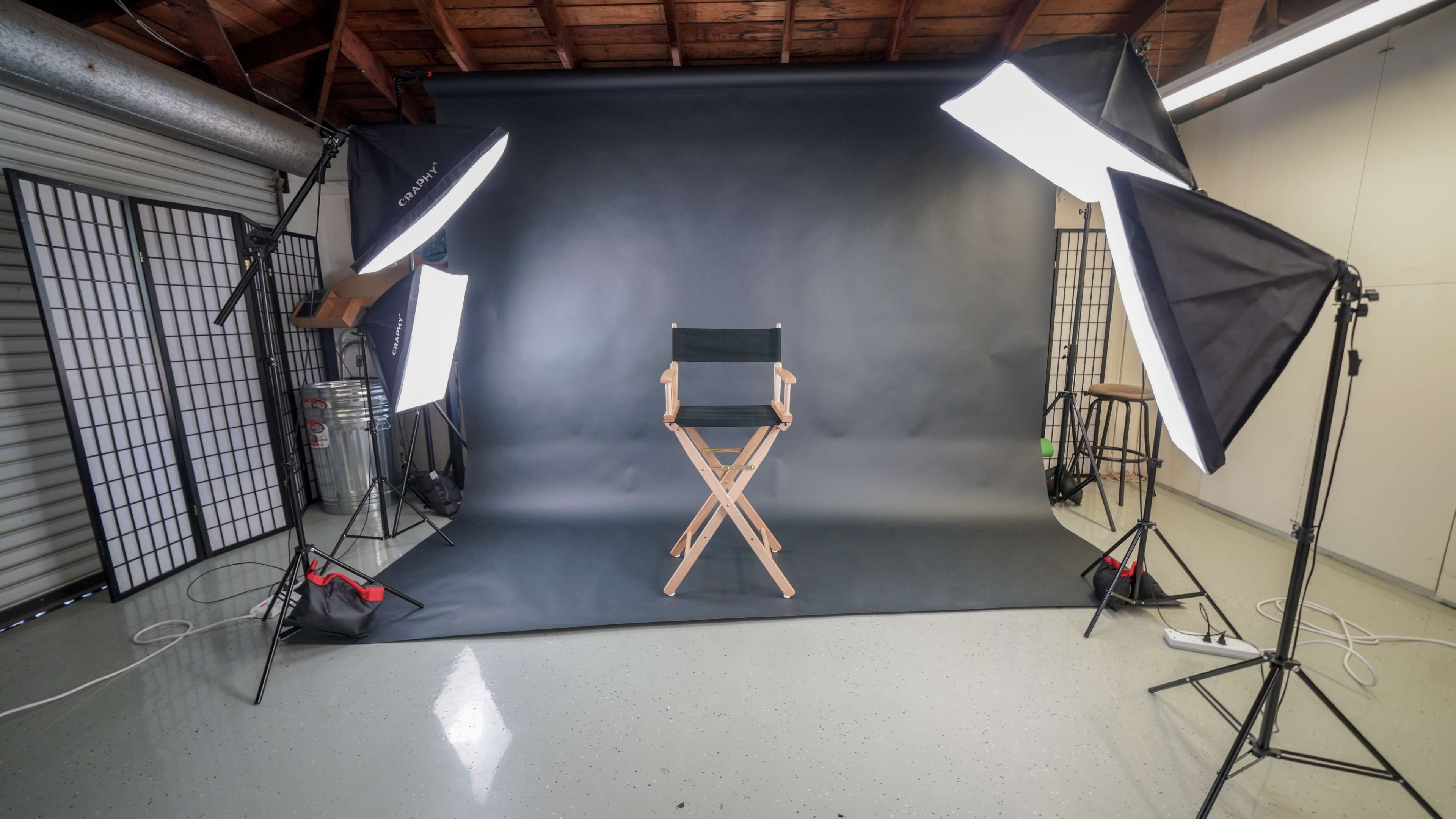 A photography studio setup with a director's chair in front of a black backdrop, illuminated by softbox lights on either side.