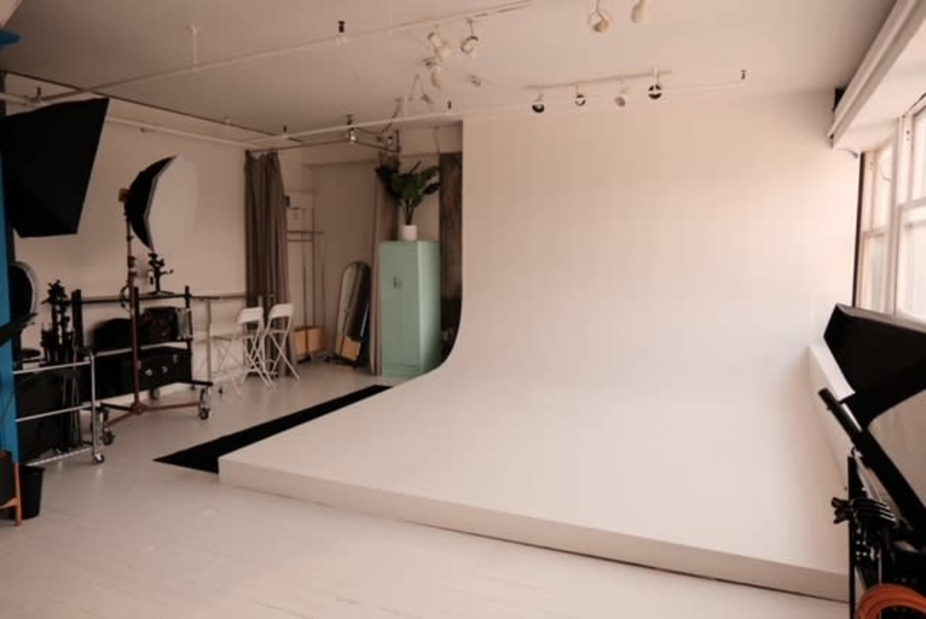 The image shows a photography studio with a seamless backdrop, lighting equipment, and a minimalistic setup.