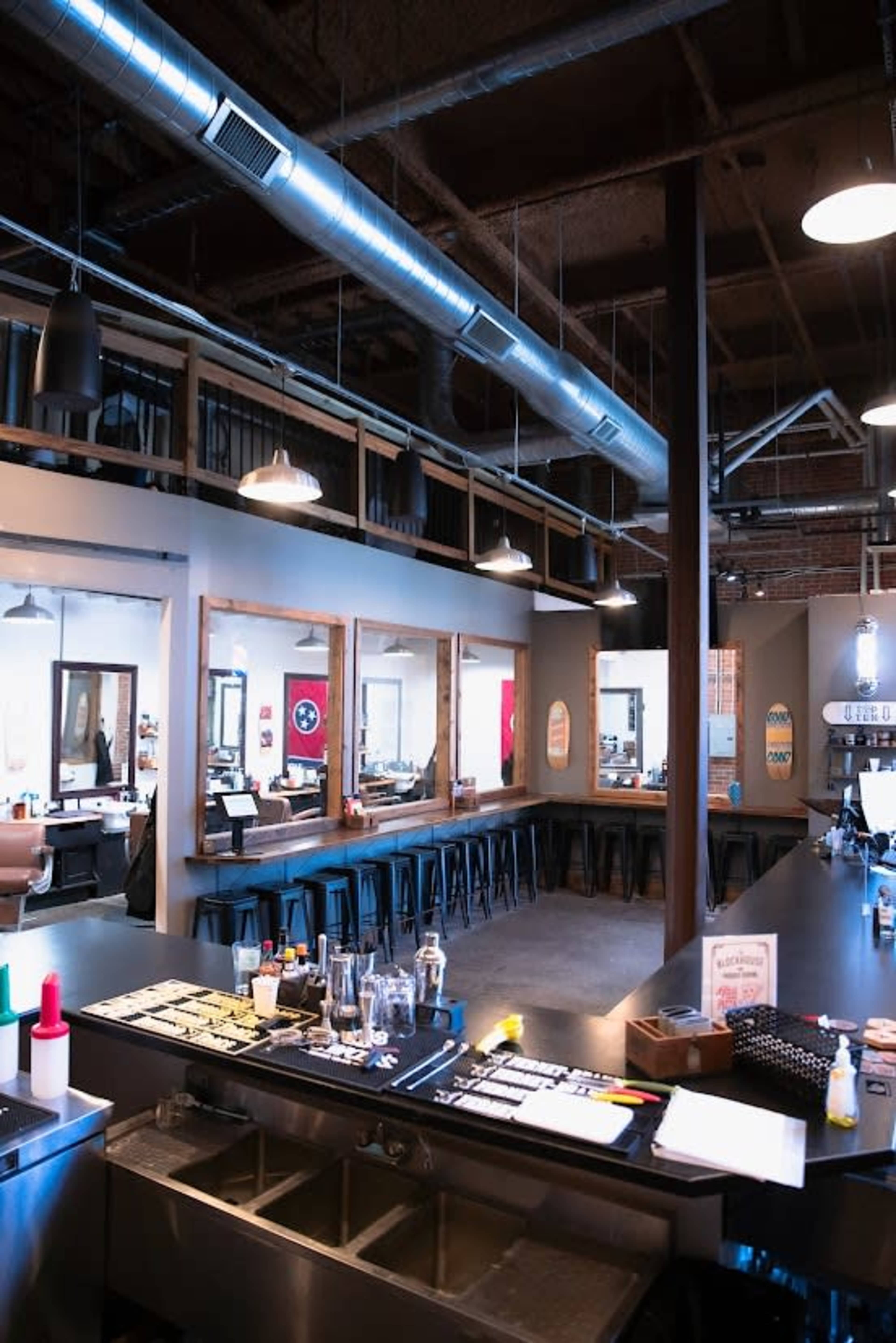 The image shows the interior of a modern barbershop with a long counter, stools, and mirrors lining the walls.