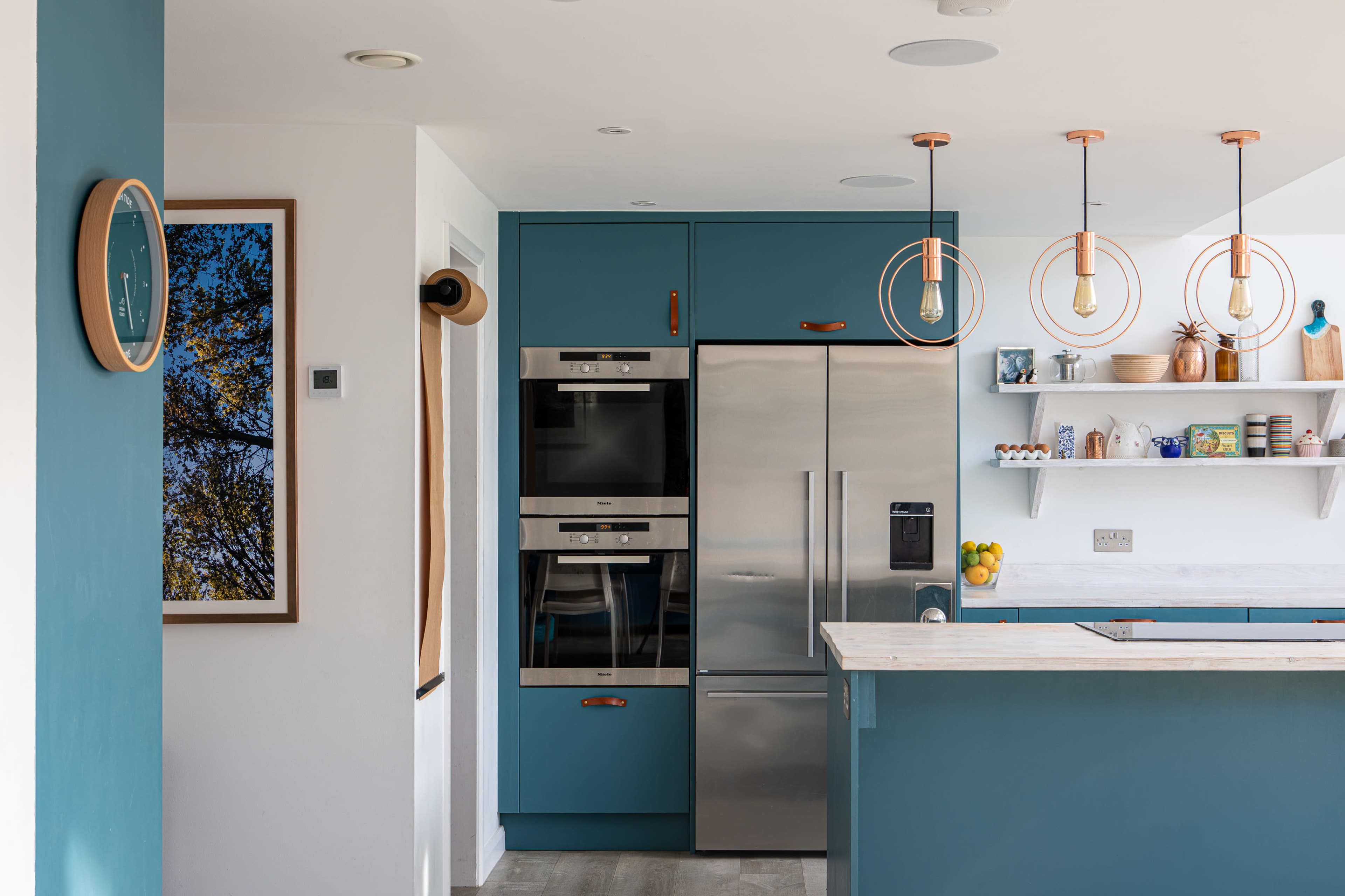 The kitchen features turquoise cabinetry, stainless steel appliances, and modern pendant lighting over a marble countertop.