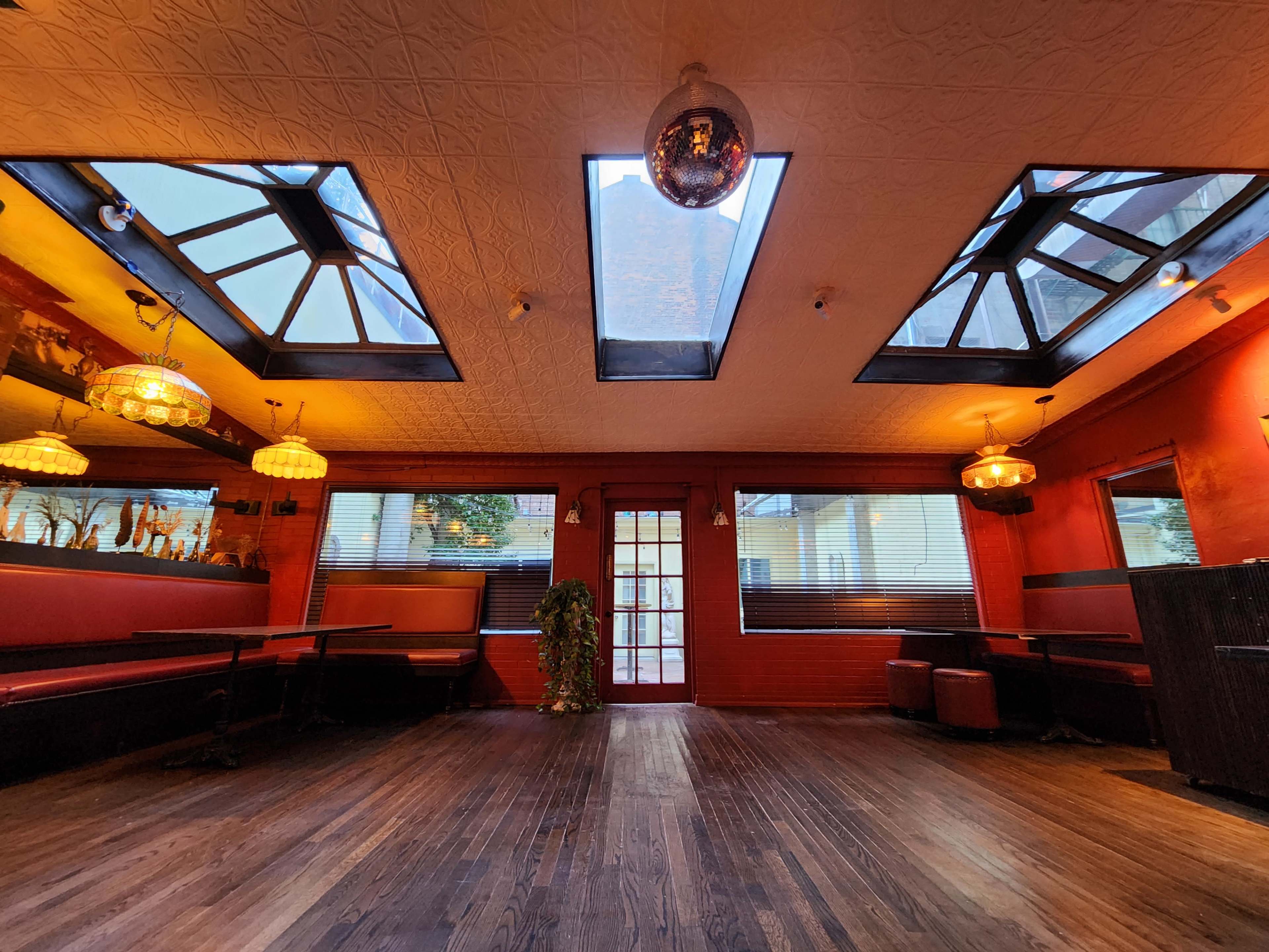 The image shows the interior of a restaurant featuring large skylights, red walls, wooden flooring, and a mix of seating arrangements.