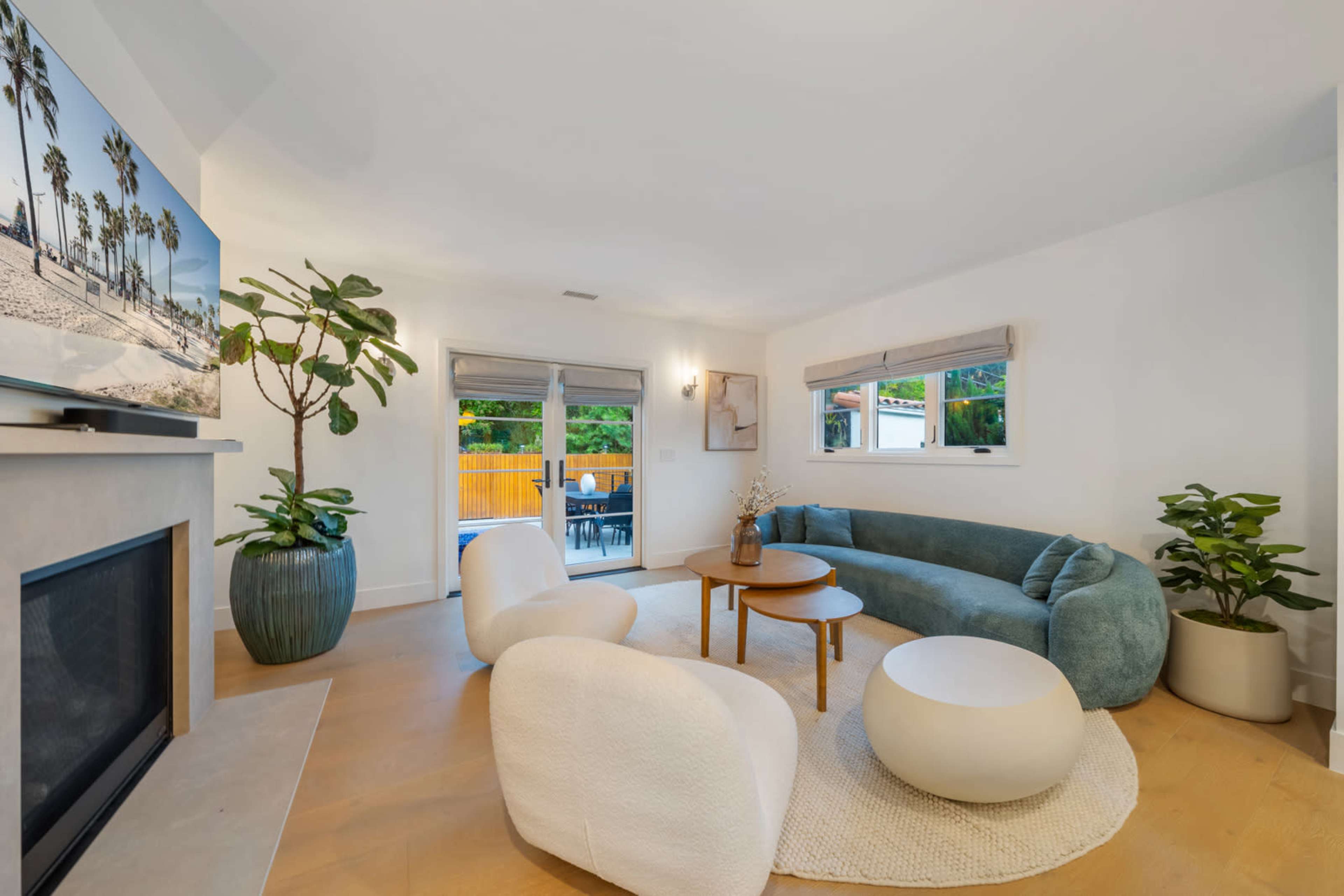 The image features a modern living room with a curved blue sofa, two white chairs, a round coffee table, and a large window overlooking a patio.