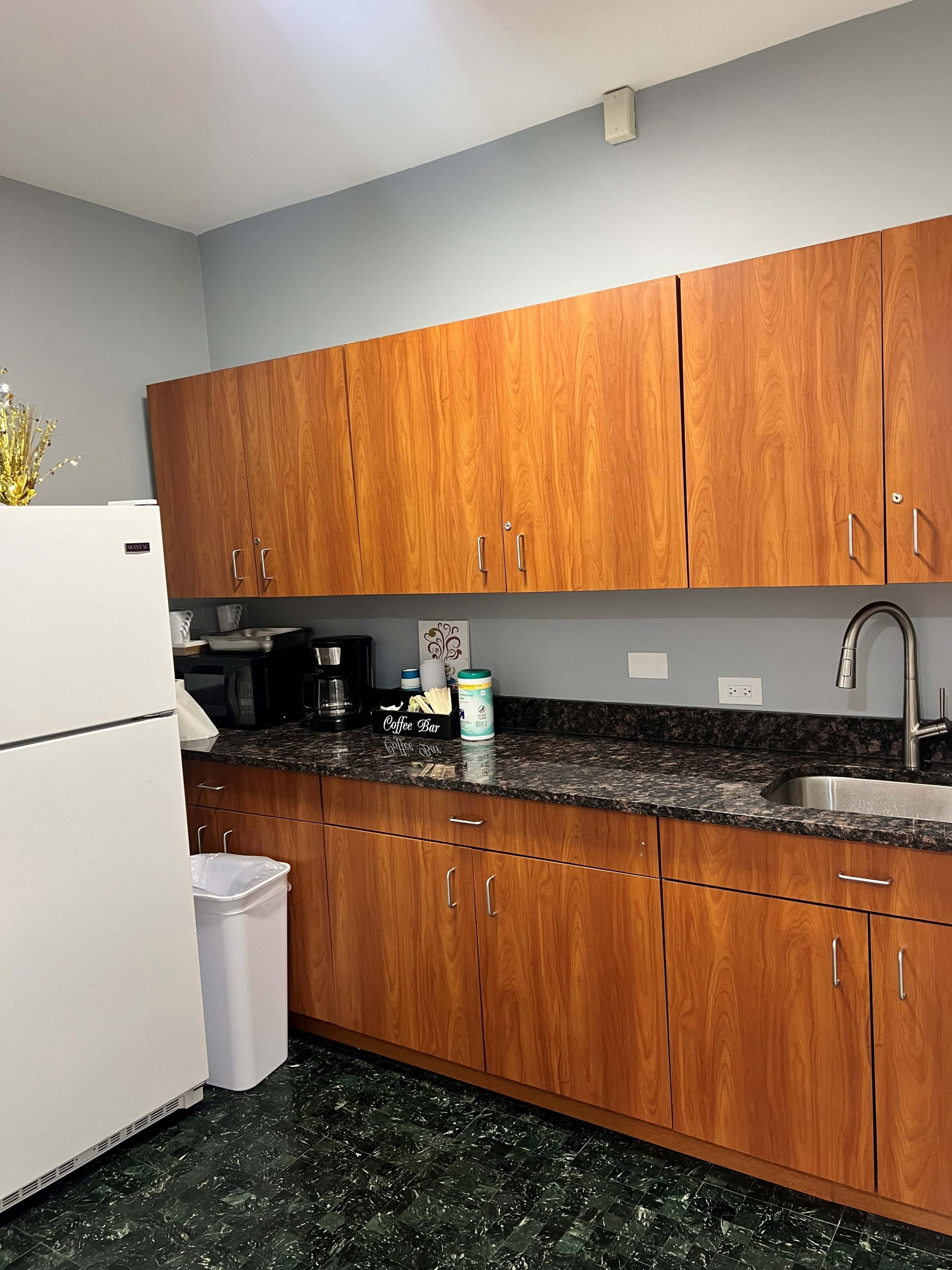 A kitchen with wooden cabinets, a stainless steel sink, and a countertop featuring a coffee maker and several containers.