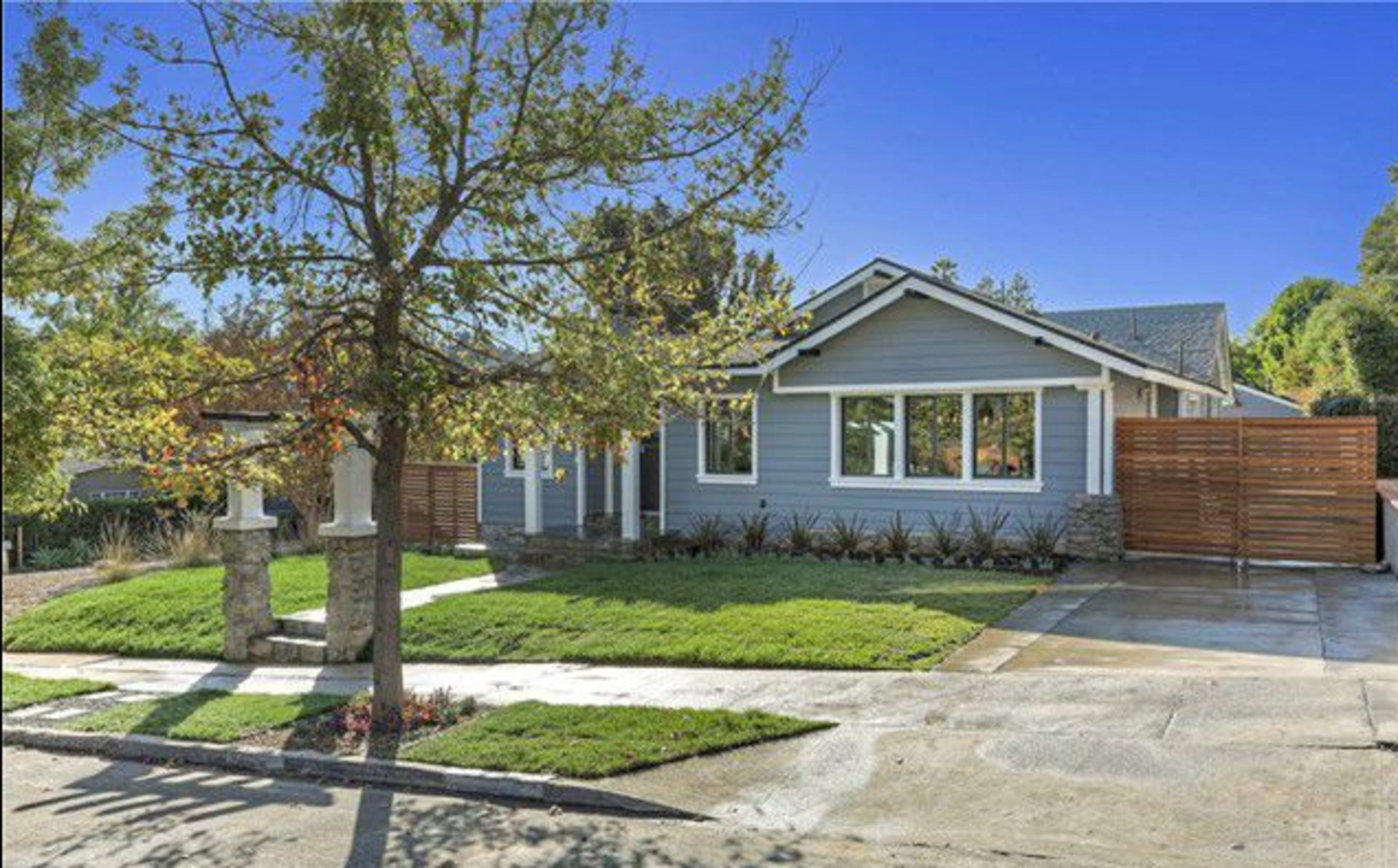 A single-story house with a landscaped front yard features a grey exterior and a wooden fence.