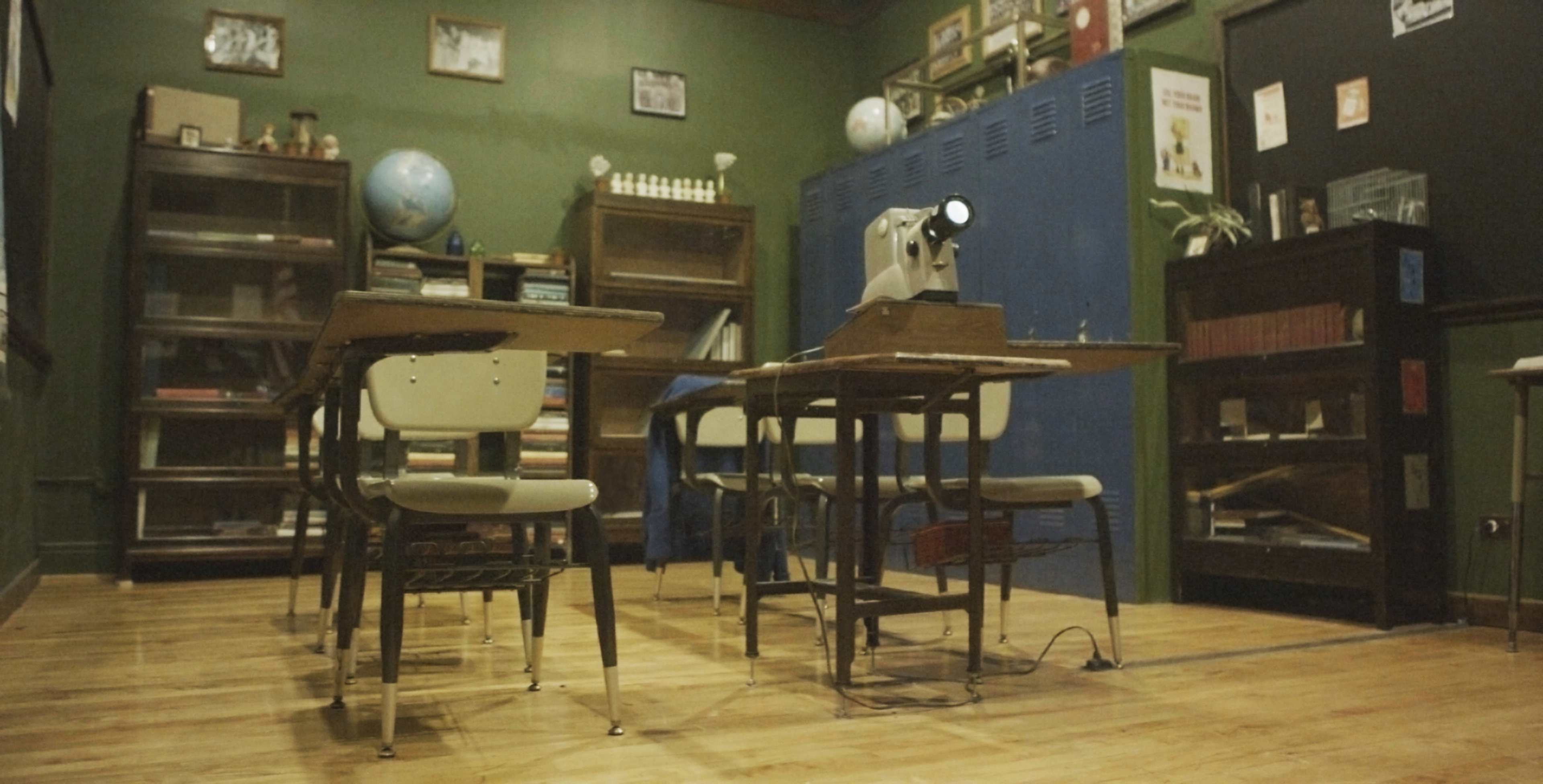 A vintage classroom setup with wooden desks, a globe, a sewing machine, and shelves filled with books.