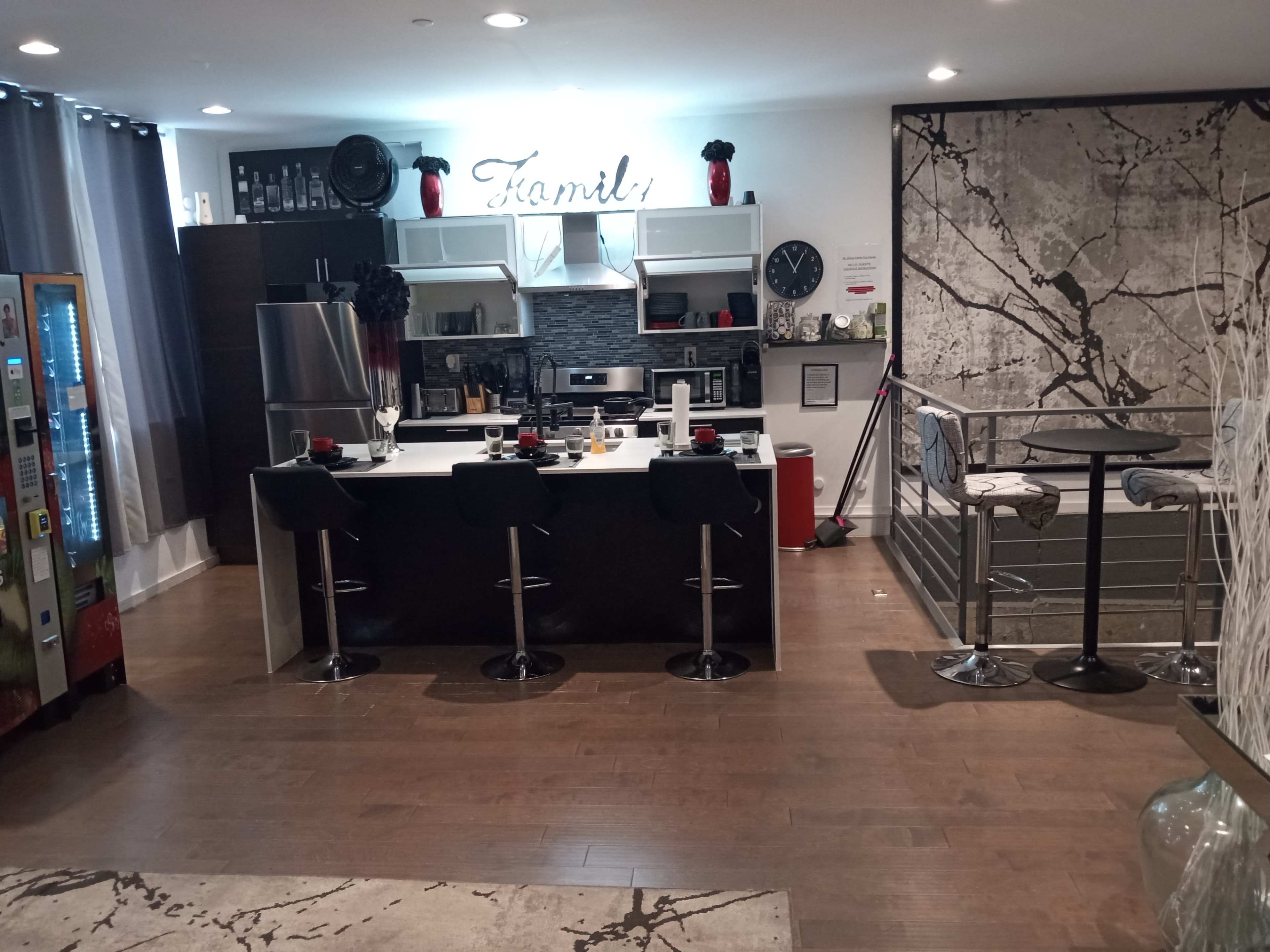 The image shows a modern kitchen and dining area featuring a bar counter with stools, a black and white color scheme, and sleek appliances.