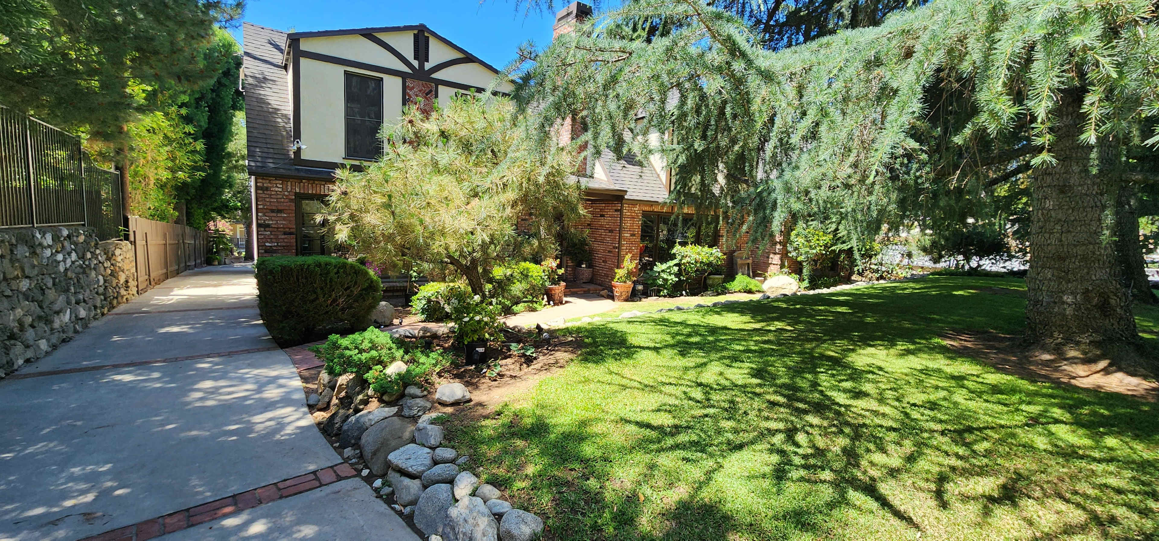 The image shows a brick house with a sloped roof, surrounded by greenery and a pathway leading to the entrance.