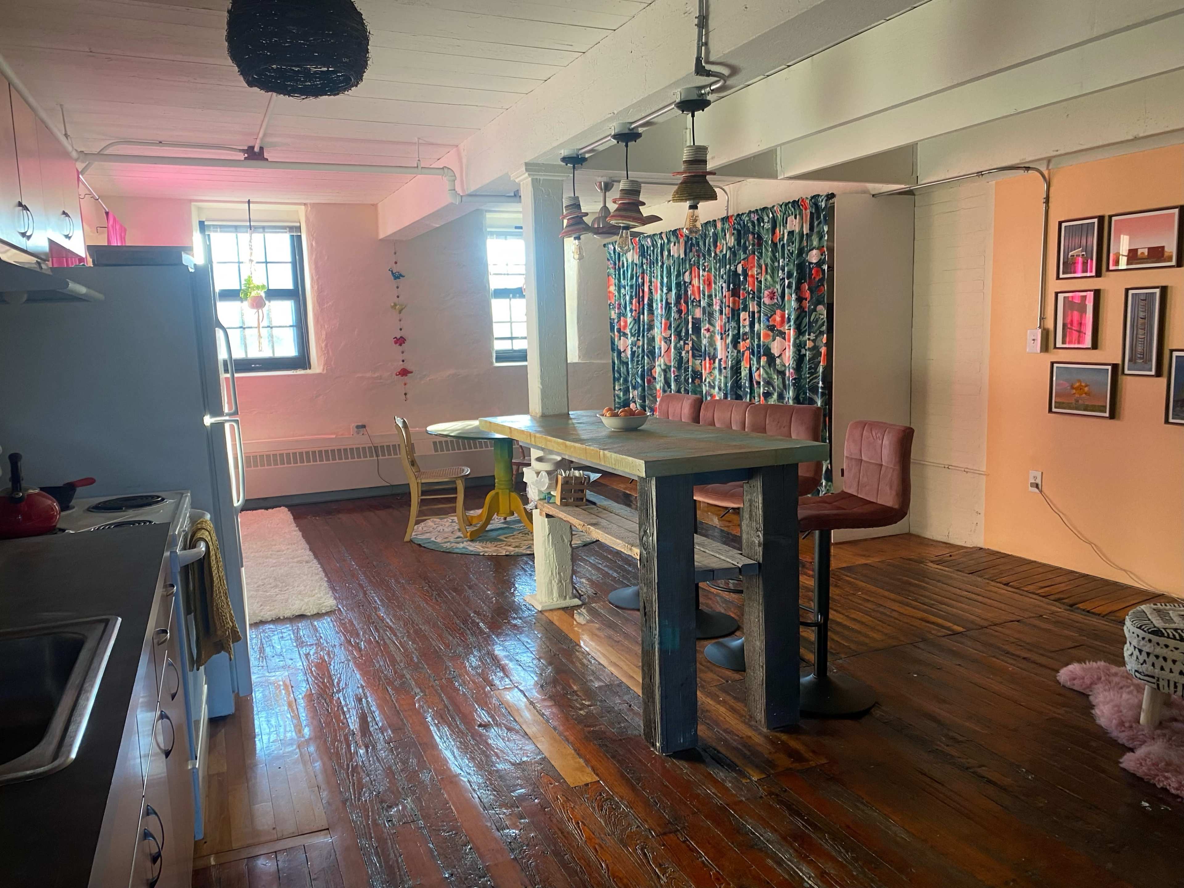 A spacious interior with a kitchen area on the left, a dining table in the center, and a decorated wall with colorful artwork in the background.