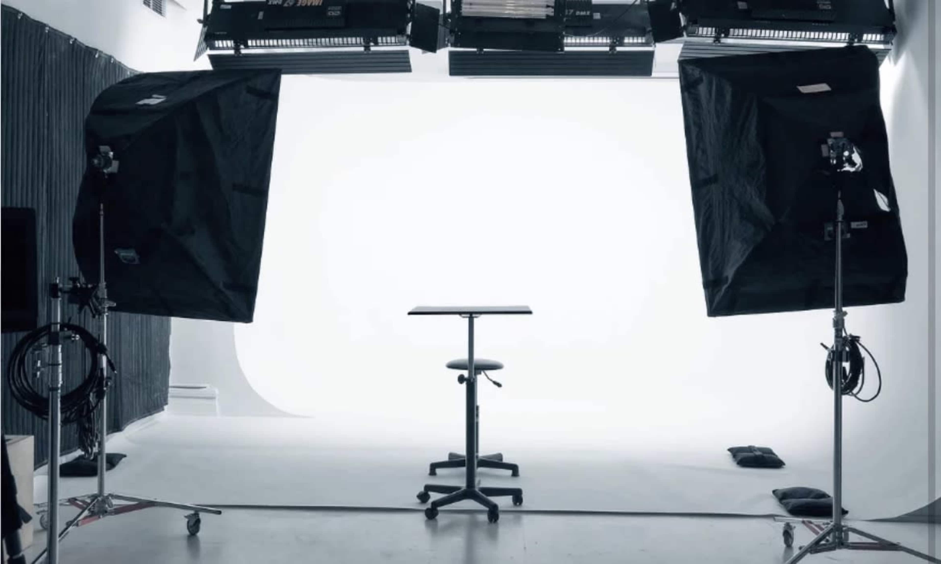 A photography studio features a bare table under bright lights with a plain white backdrop.