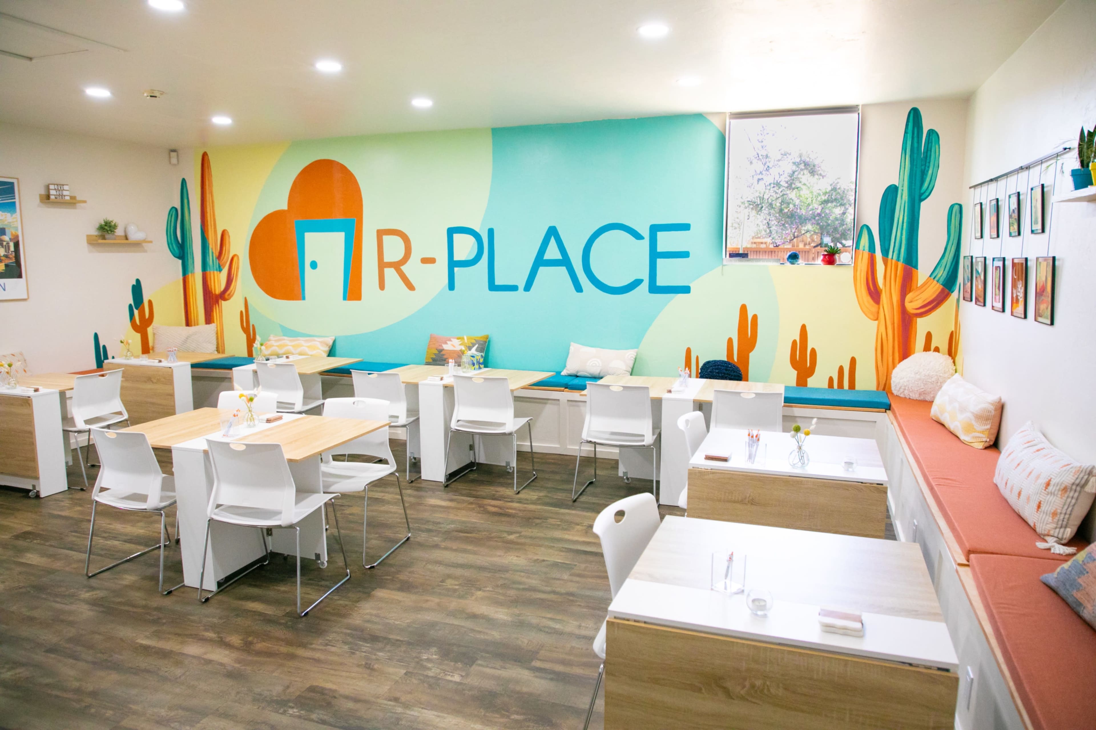 A brightly decorated café with a mural on the wall and various seating arrangements, including tables and a cushioned seating area.